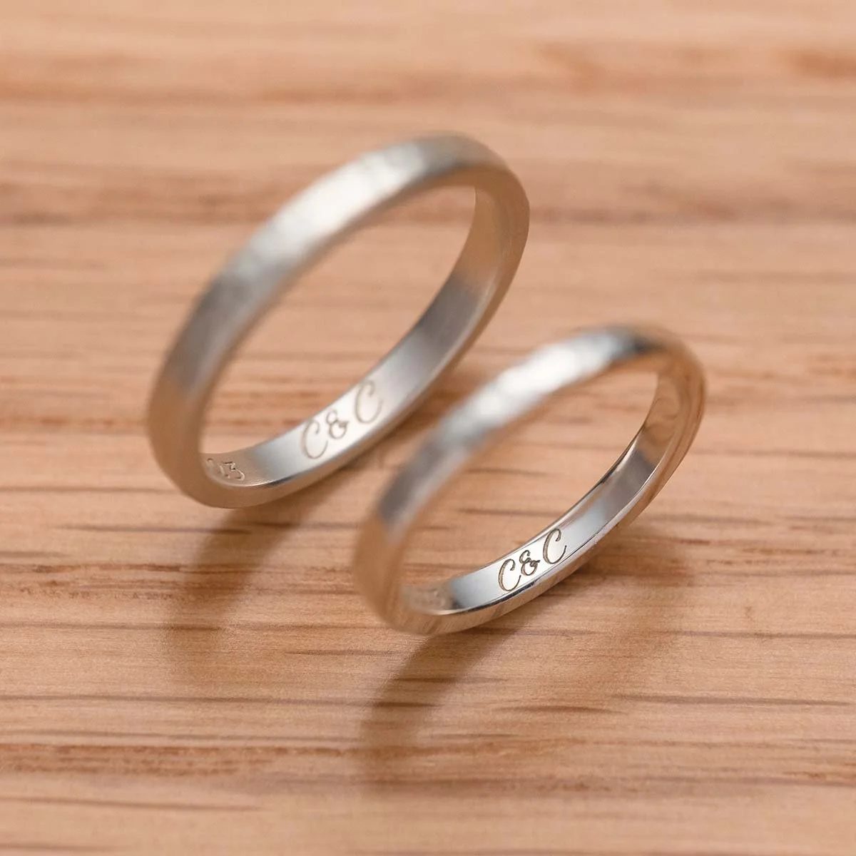 Two laser engraved sliver ring on wooden texture table