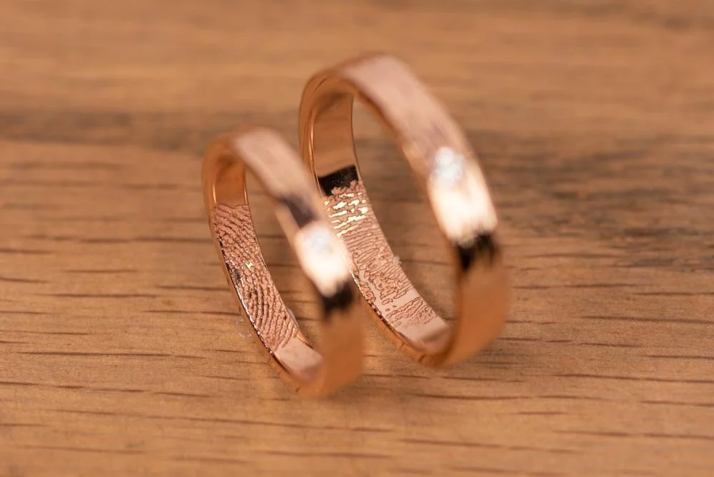 Two Rose Gold Fingerprint Engraved Ring on wooden table