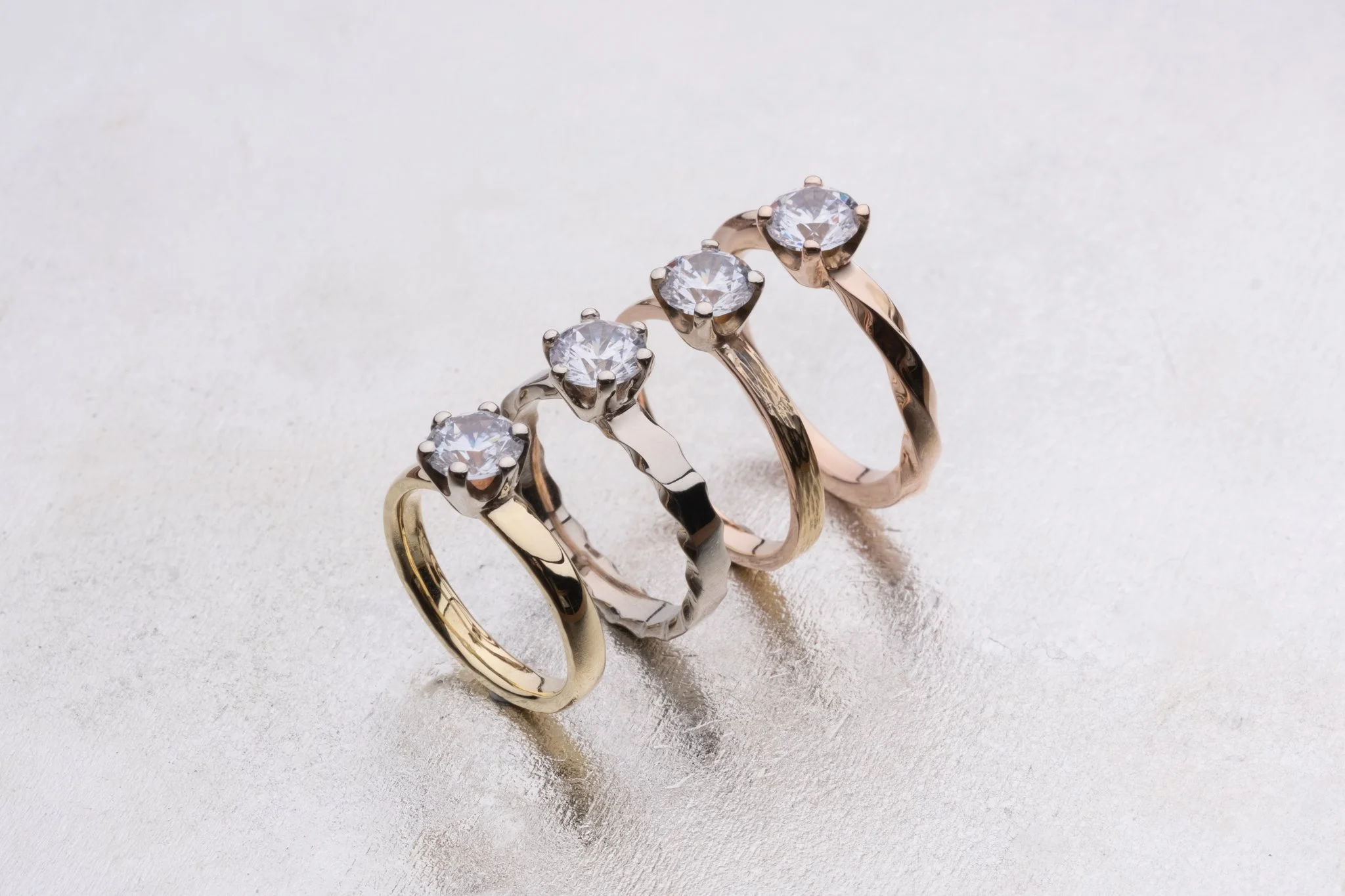 Close-up of 4 engagement rings with different patterns and materials on a silver surface
