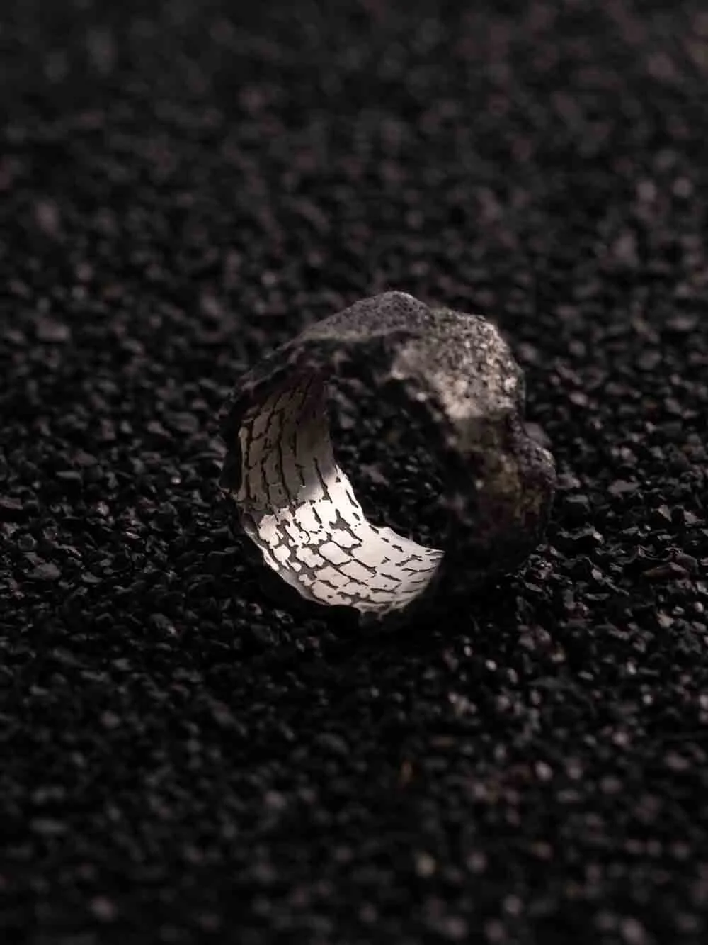 Side view of 2073 City Decay annihilate ring with stone wall texture placed on back sand