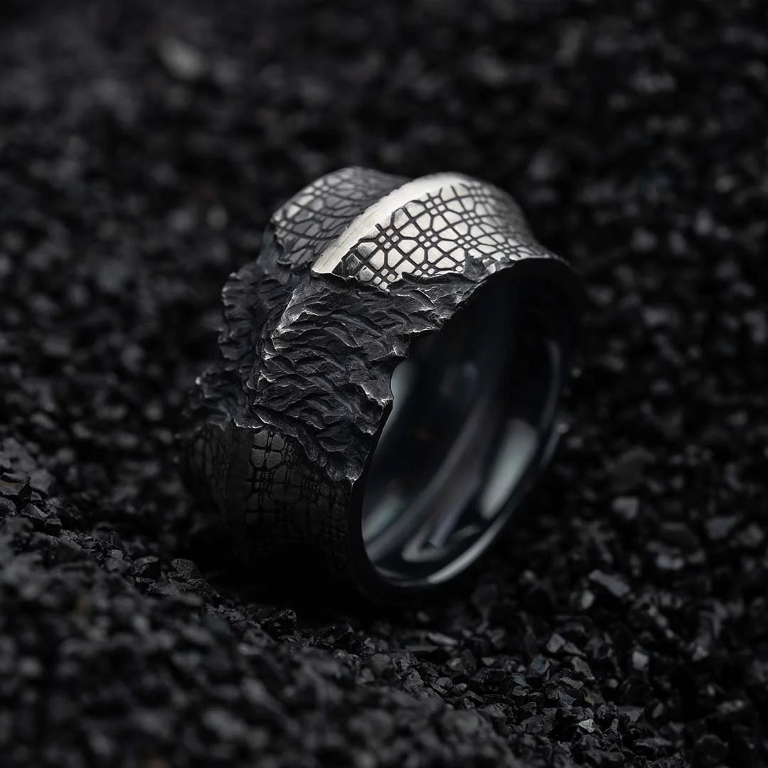 Angled view of the 2073 City Decay Decay ring with a cracked mosaic pattern, placed on black coal