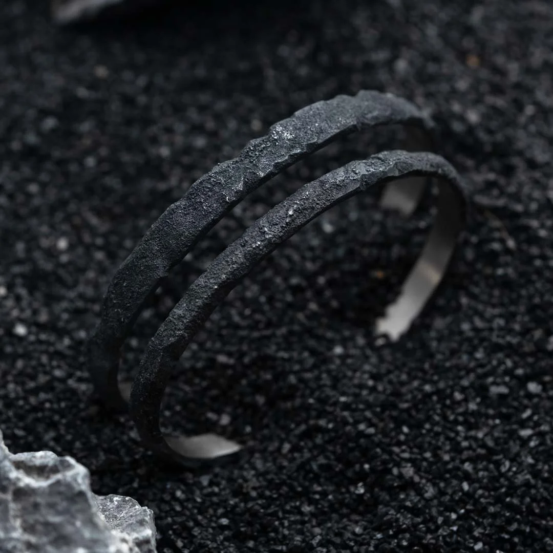 Close-up of two 2073 City Decay Stardust bracelet in black raw surface on black sand