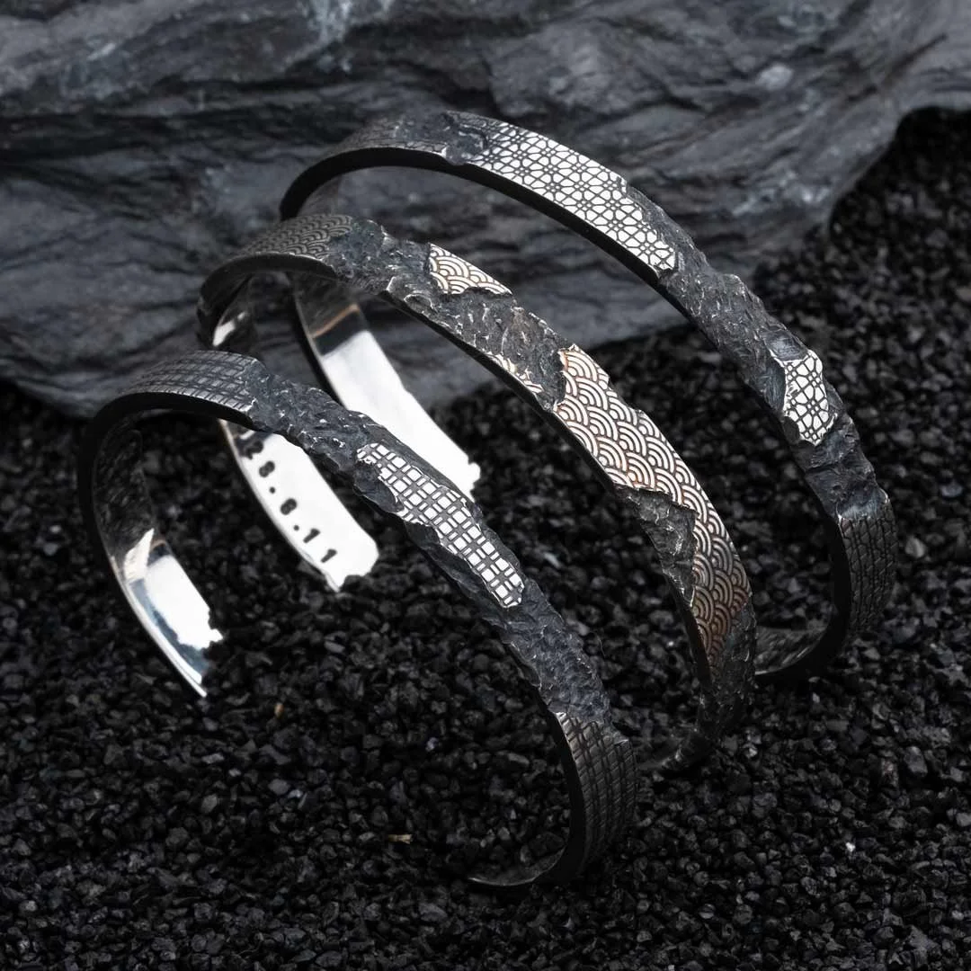 Three 2073 City Decay Collapse bracelet with mosaic patterns and charred textures, arranged on black coal