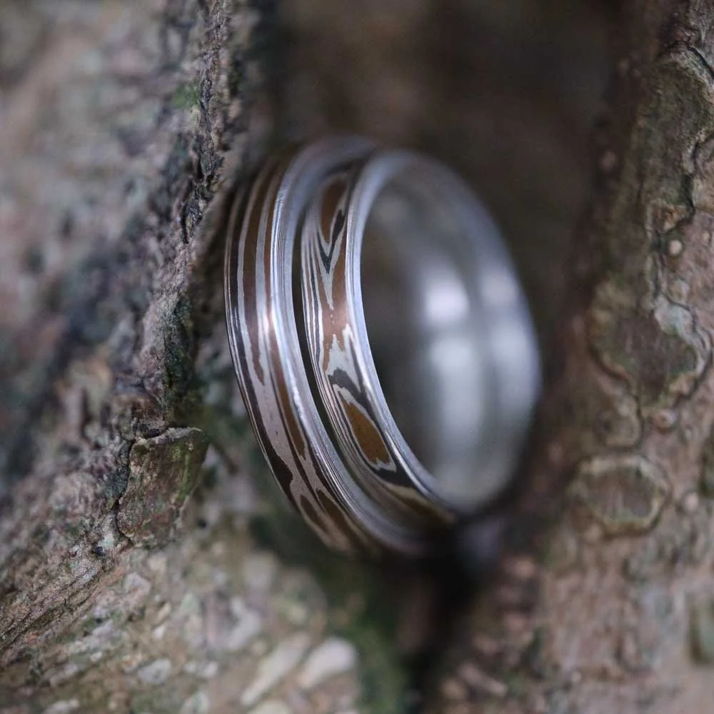 Two Silver rings with black and white pattern resting on a rough wooden surface.