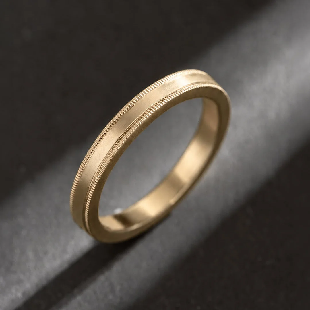 Close-up view of a yellow gold milgrain ring, casting a shadow on a gray background.
