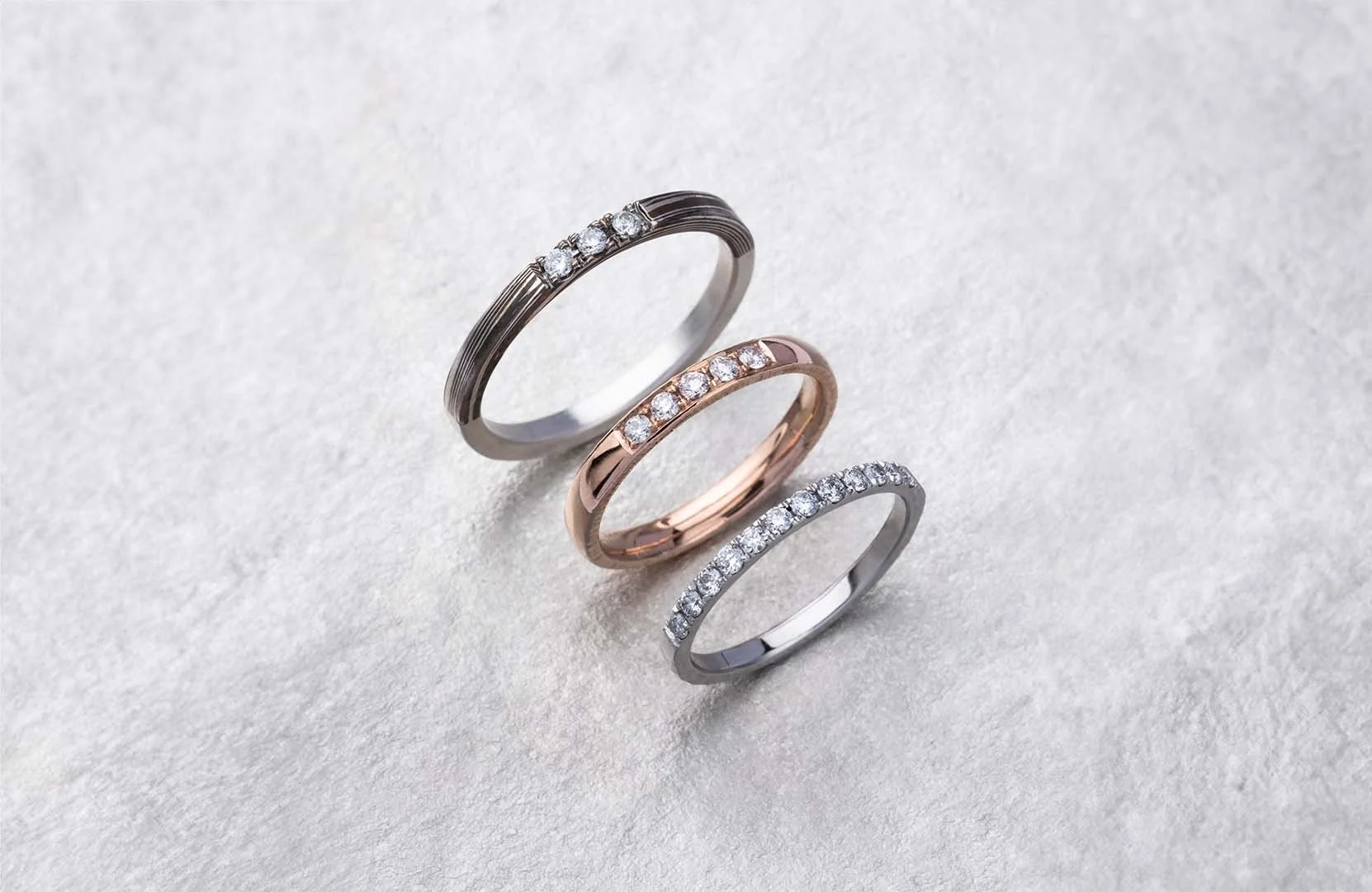 Three Rings in sliver, rose gold, and mokume gane materials with Micro Pavé Stone Setting placed on a sliver surface