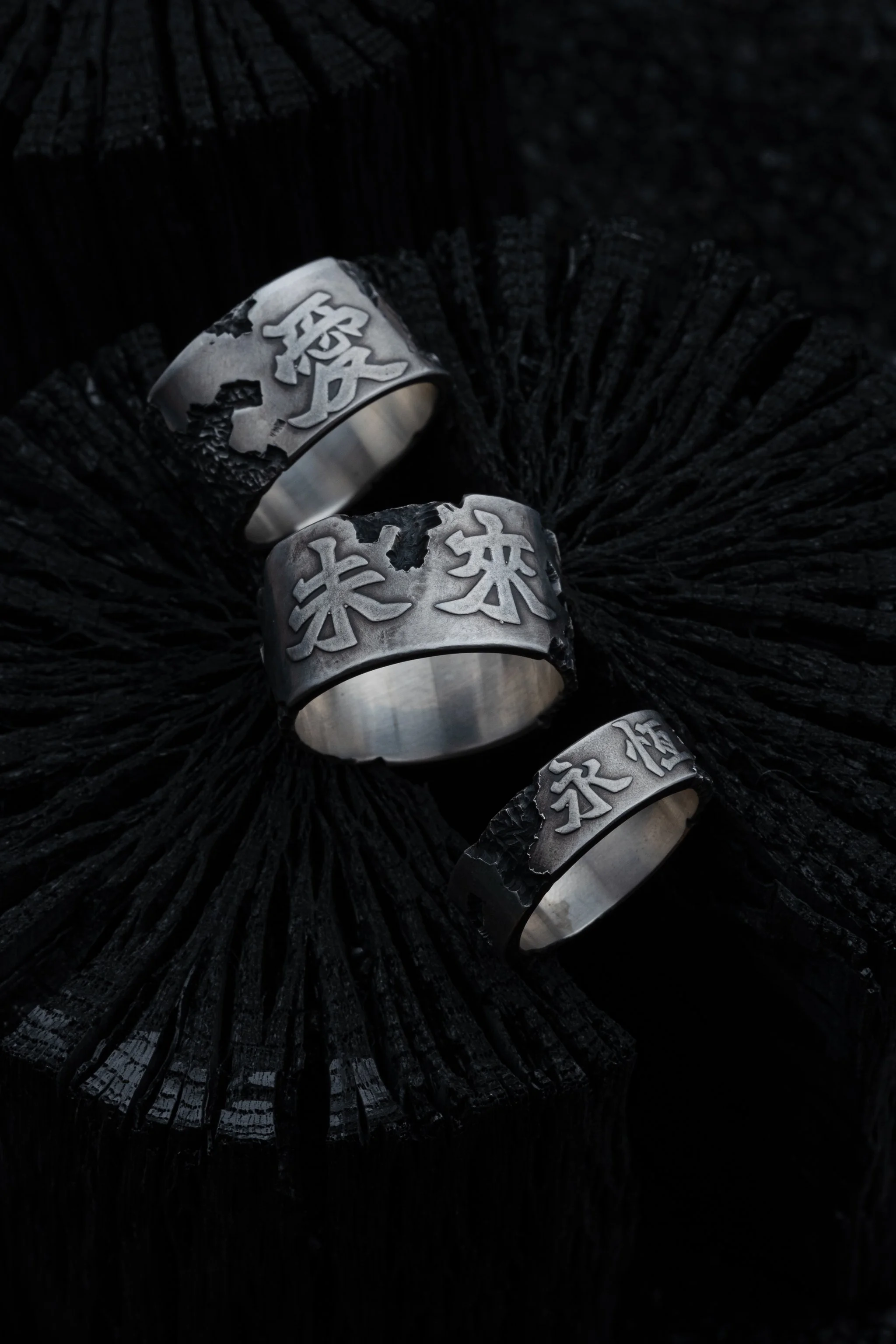 Three silver rings from 2073 City Decay X Zansyu collection placed on a coal in dark background