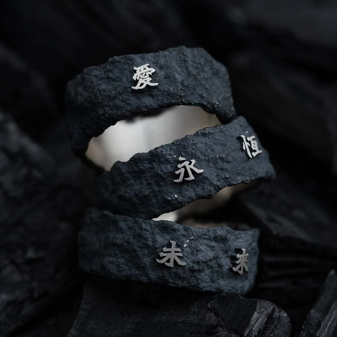 Close-up of three Ember Rings from the 2073 City Decay Collection, each engraved with different Chinese phrases and meanings, stacked together on coal
