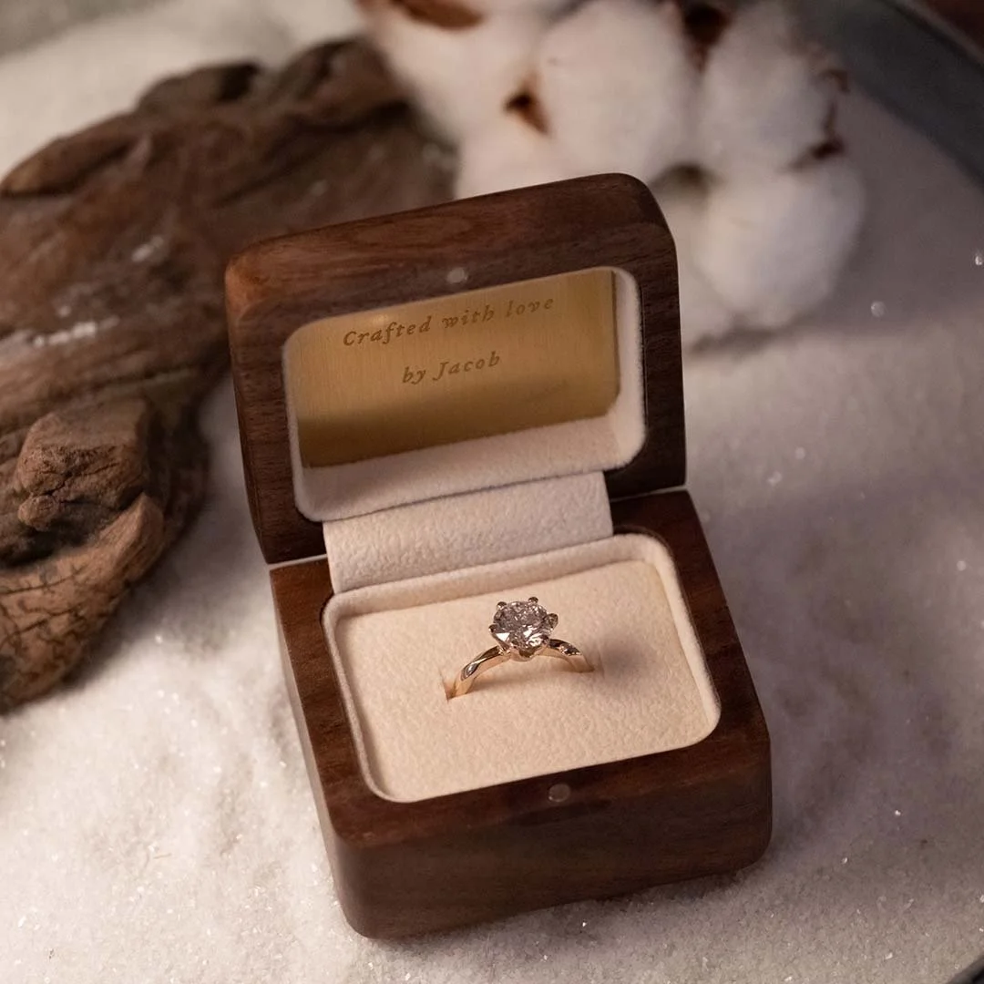 A wood wedding ring box on white sand with wood and cotton flower behind