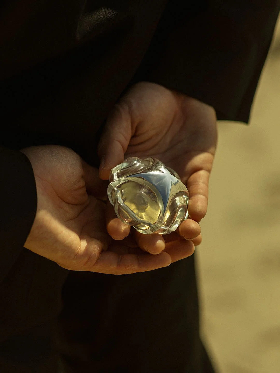 Man in black suit holding a transparent ring box under nature sun lighting