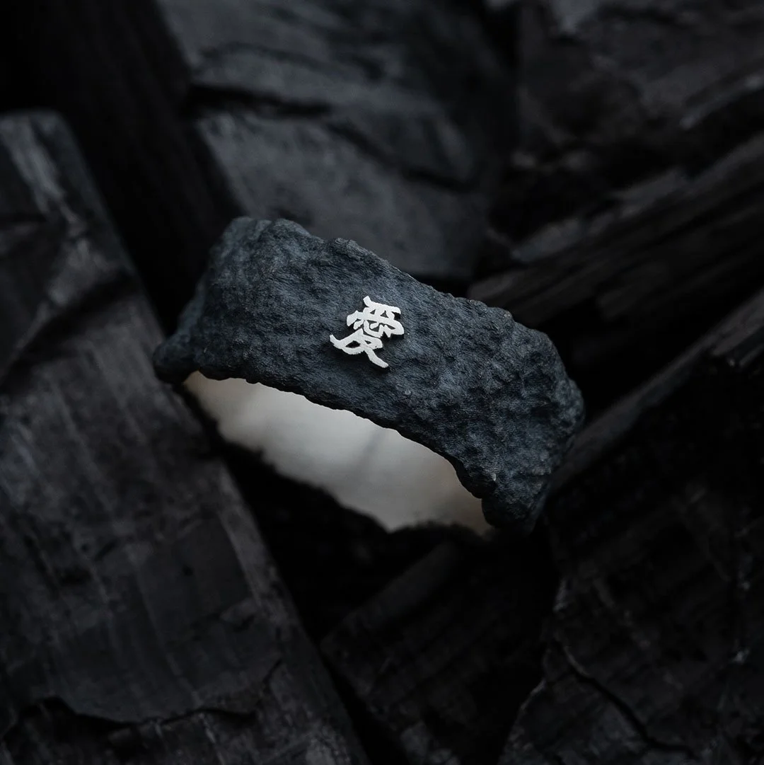 2073 City Decay Collection Ember Ring with the chinese word meaning love engraved on the ring in black color raw texture placed on coal