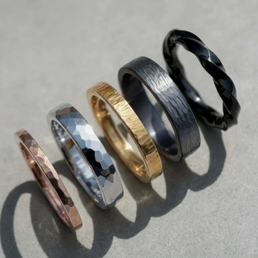 A collection of five rings with different finishes and colors arranged in a row on a neutral surface, casting shadows.