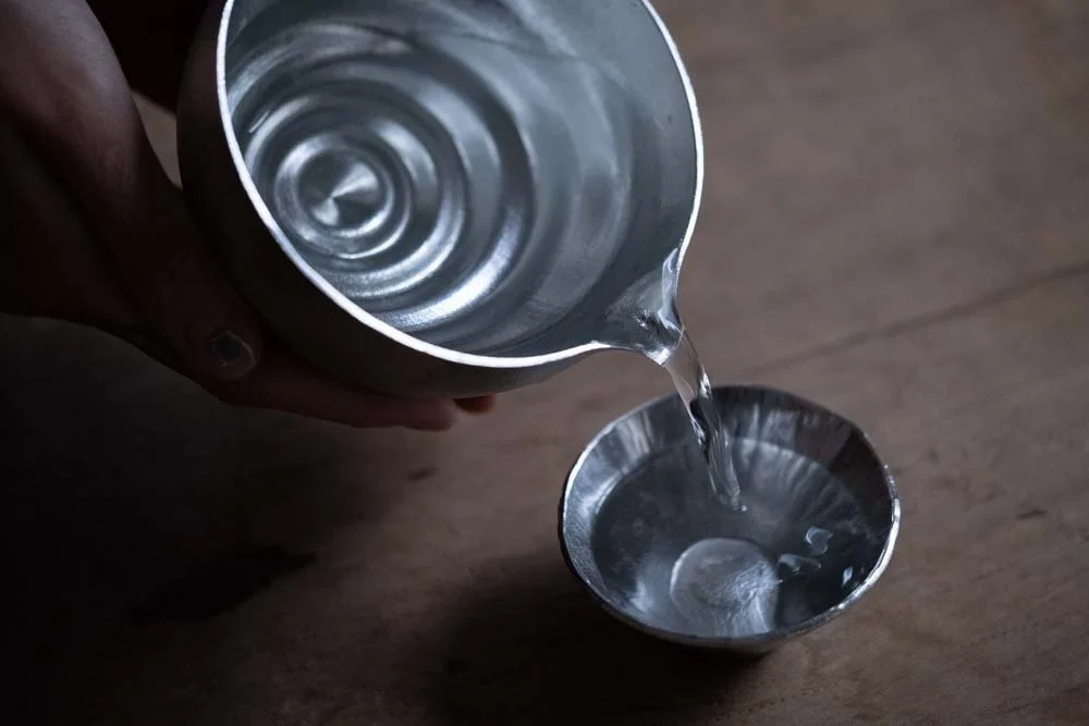 a pure tin bowl filled with sake pouring sake into a pure tine sake cup