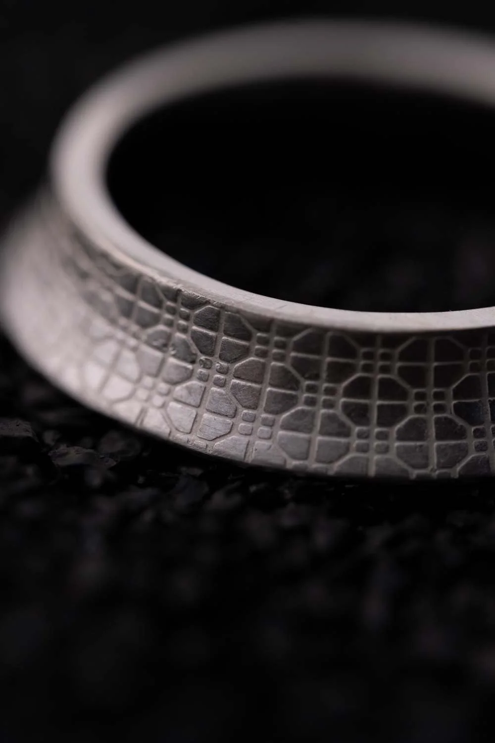 Close-up the pattern of silver ring from 2073 City Decay collection ] under black sand