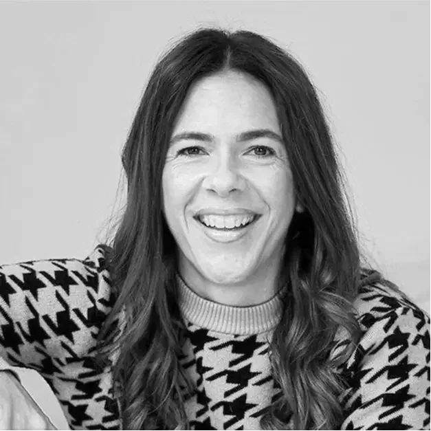 Black and white photo of a smiling woman with long, wavy hair wearing a patterned sweater.