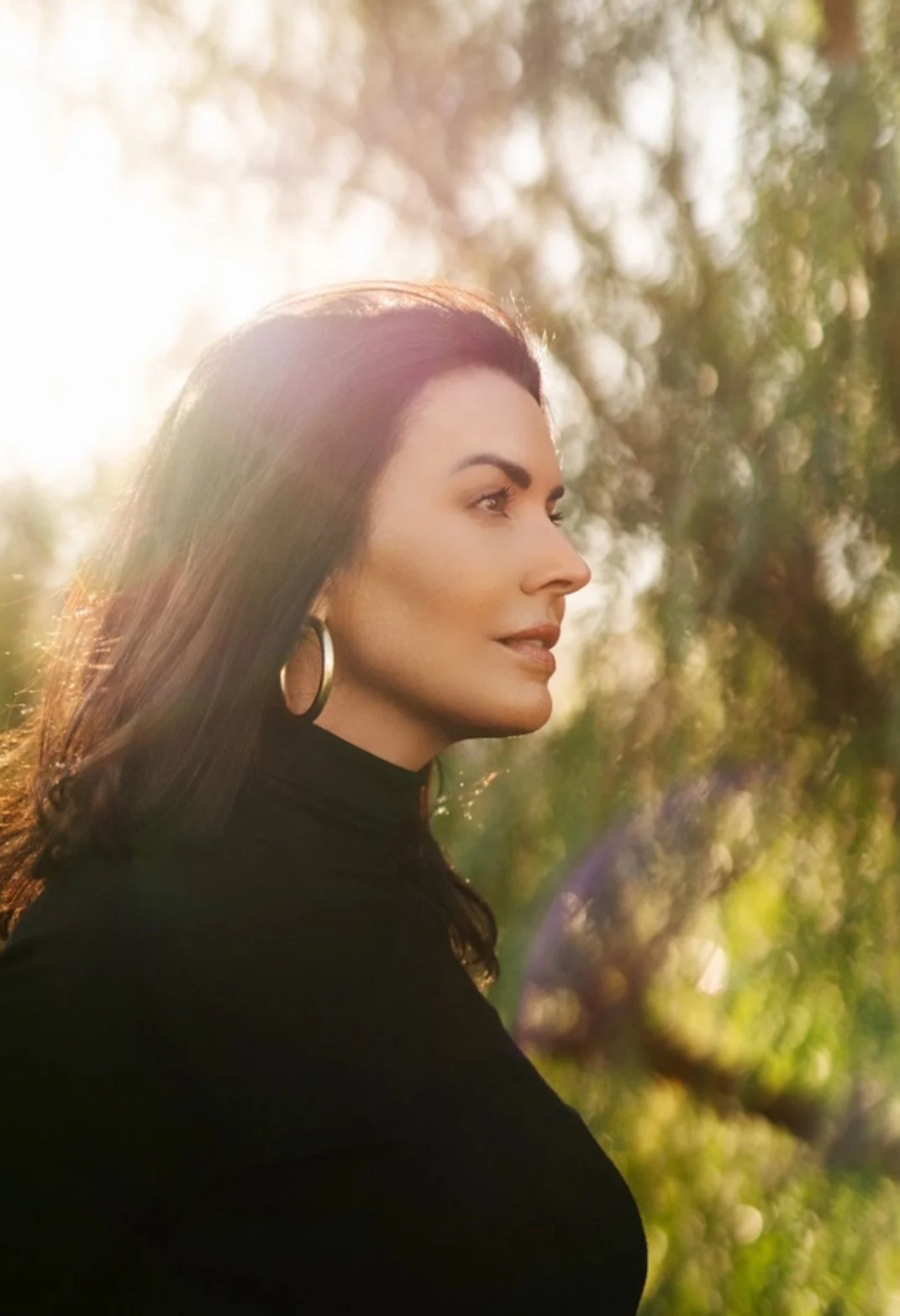 Michelle Madrid in profile, wearing black against a sunlit green landscape