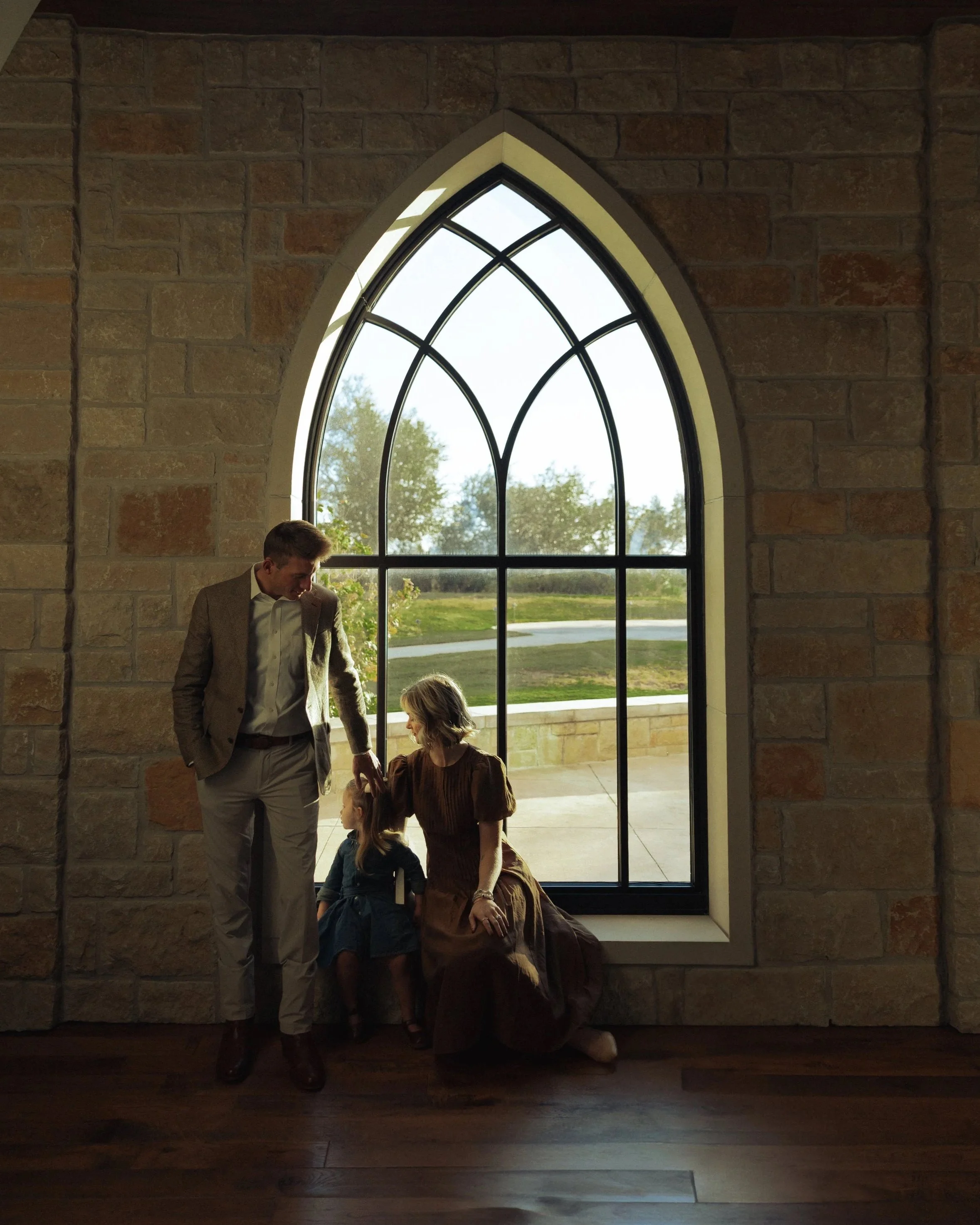 Austin Texas family photographer. Mom, dad, daughter in church chapel posing for unique family session. Beautiful light coming through window.