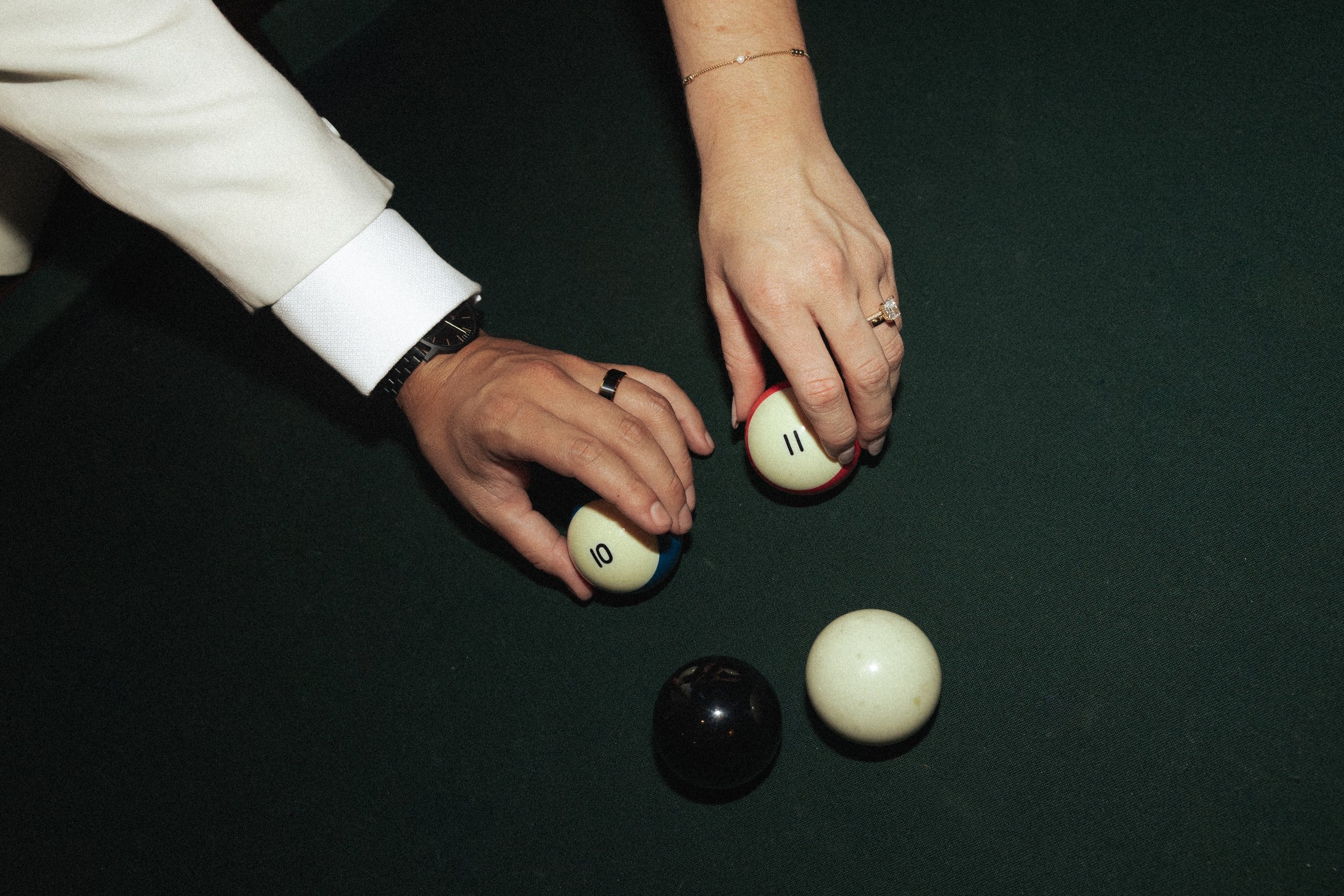 Two people playing pool, with one holding the cue ball and the other holding the 11 ball, on a green pool table.