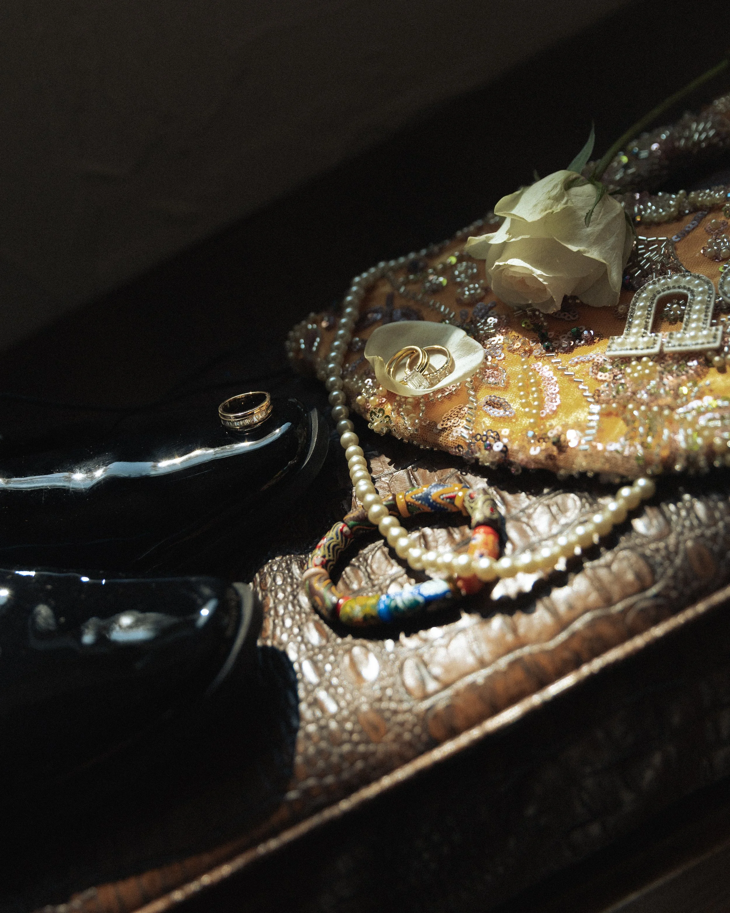 A collection of jewelry and personal items including rings, necklaces, and a flower, arranged on a fabric surface.