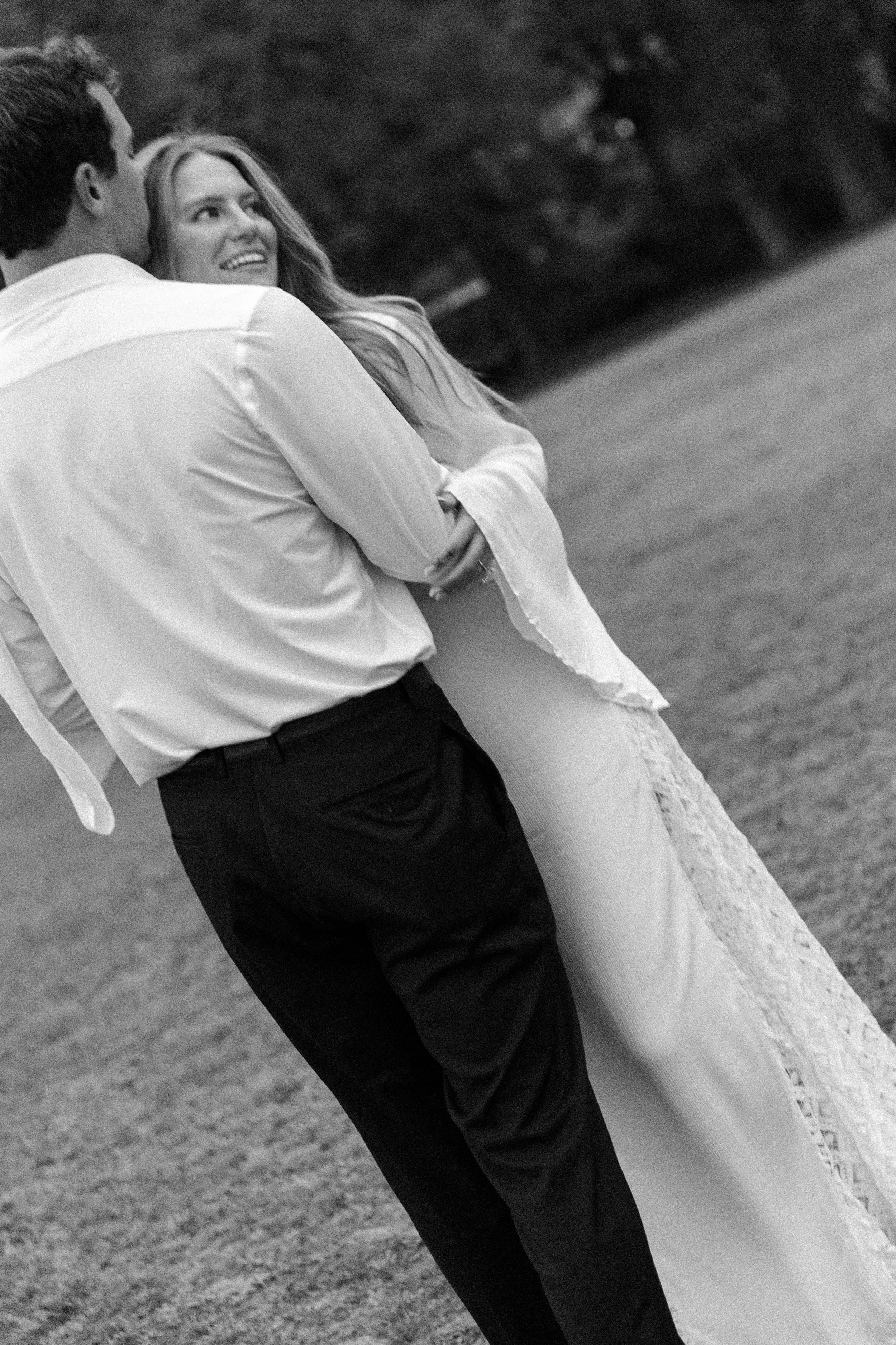 A couple dancing outdoors at sunset with trees in the background, captured in black and white.