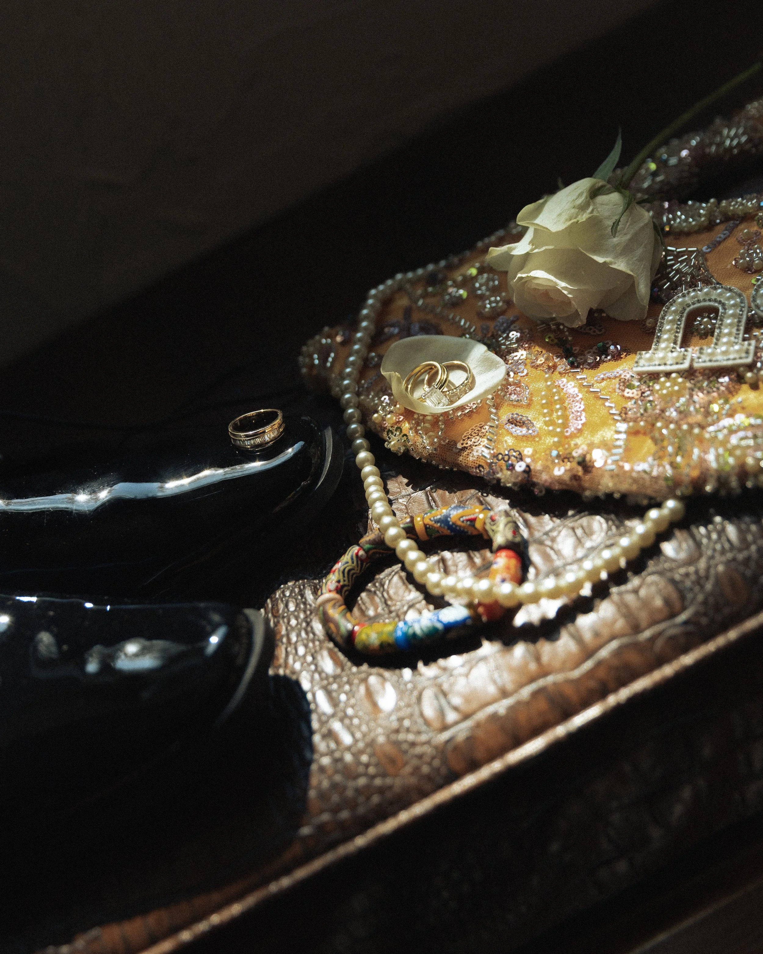 Jewelry and a white rose on a colorful, embellished fabric surface.