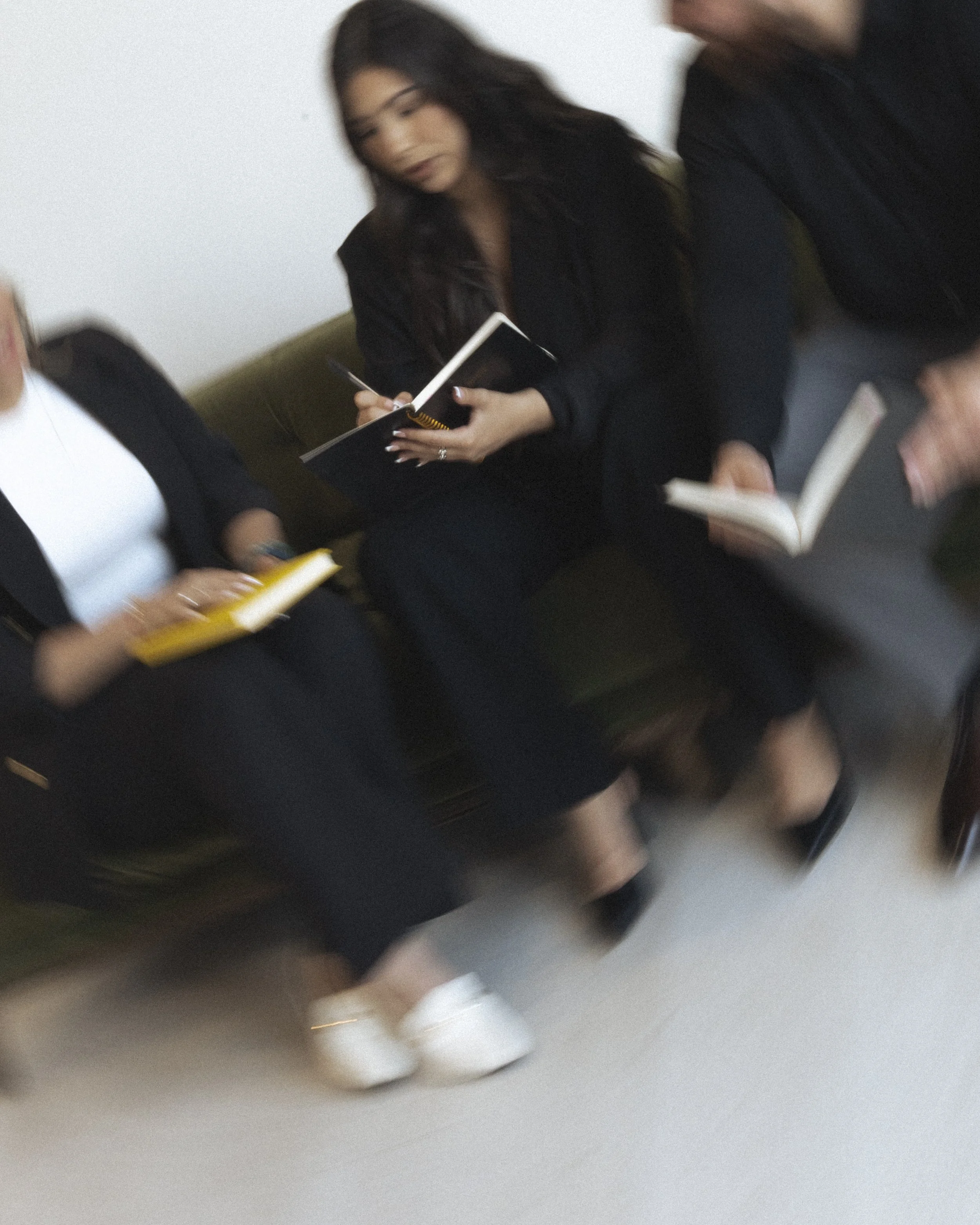 Three women sitting on a bench, engaged in conversation and reading books in a casual setting.