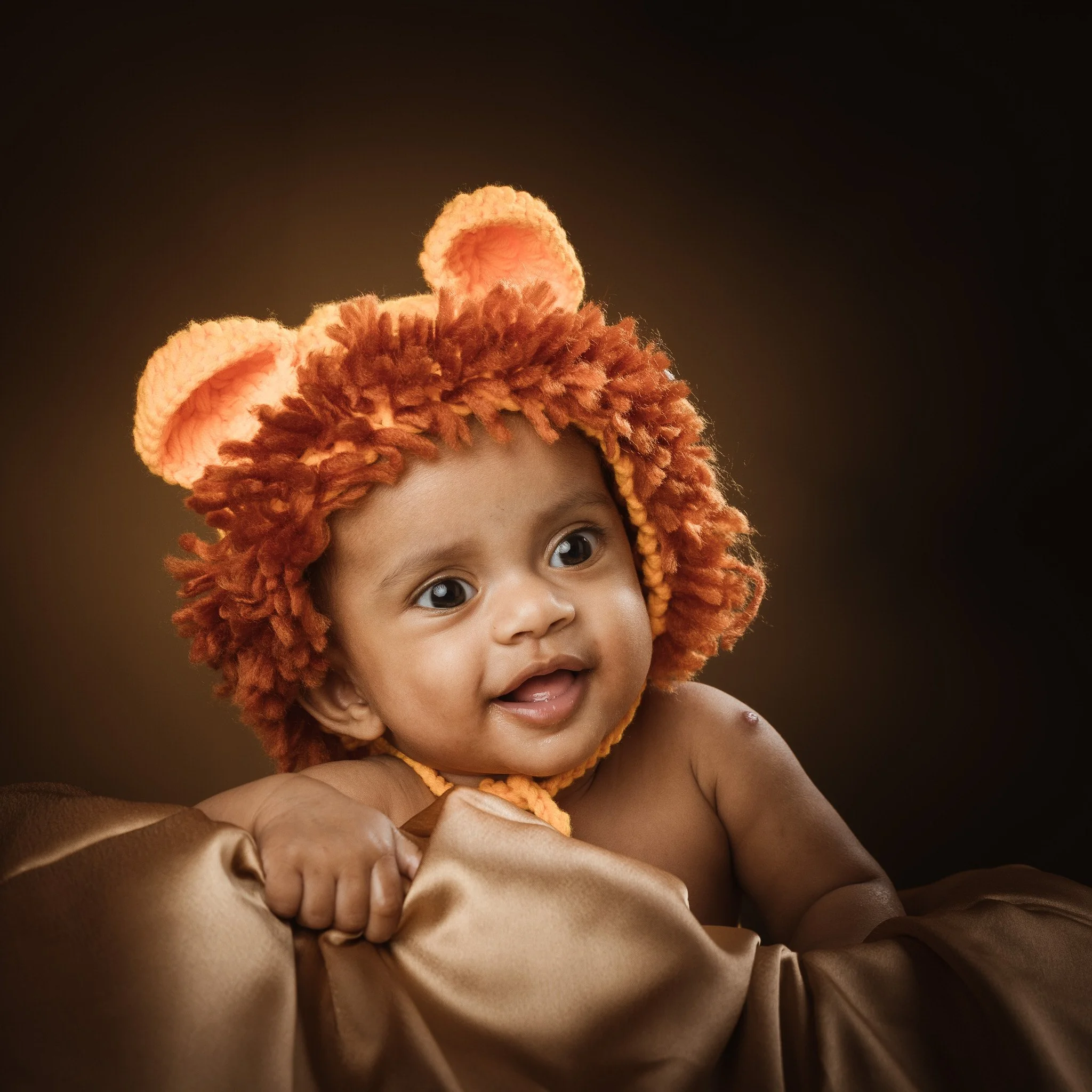 A baby with curly hair wearing a lion costume hat with ears, smiling and looking to the side, against a dark background.