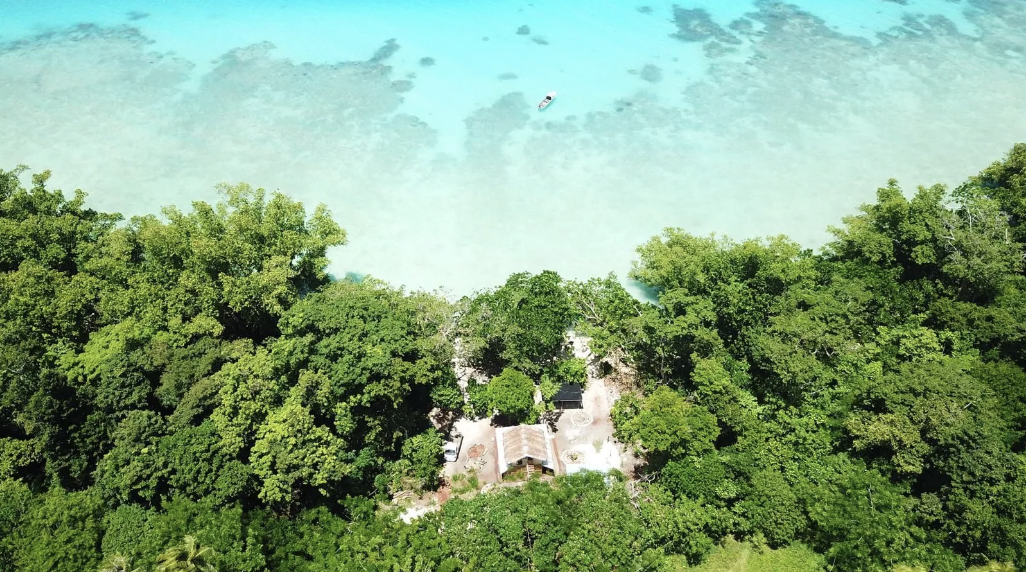 Aerial view of a tropical beach with clear turquoise water, dense green trees, and a small building near the shoreline. Beach Front on Aore Accomodation / Airbnb