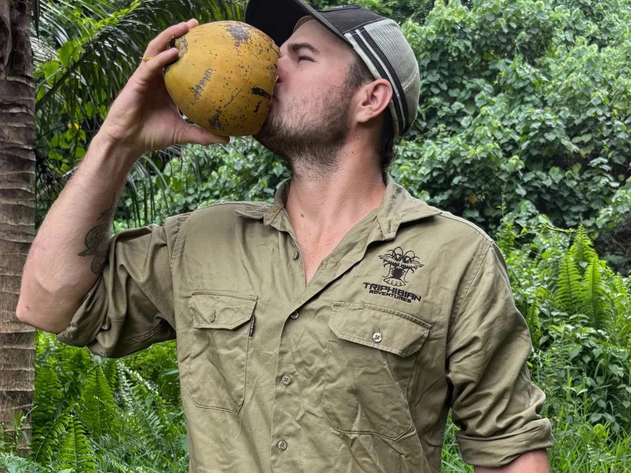 Xande wearing a triphibian khaki work shirt drinking a coconut