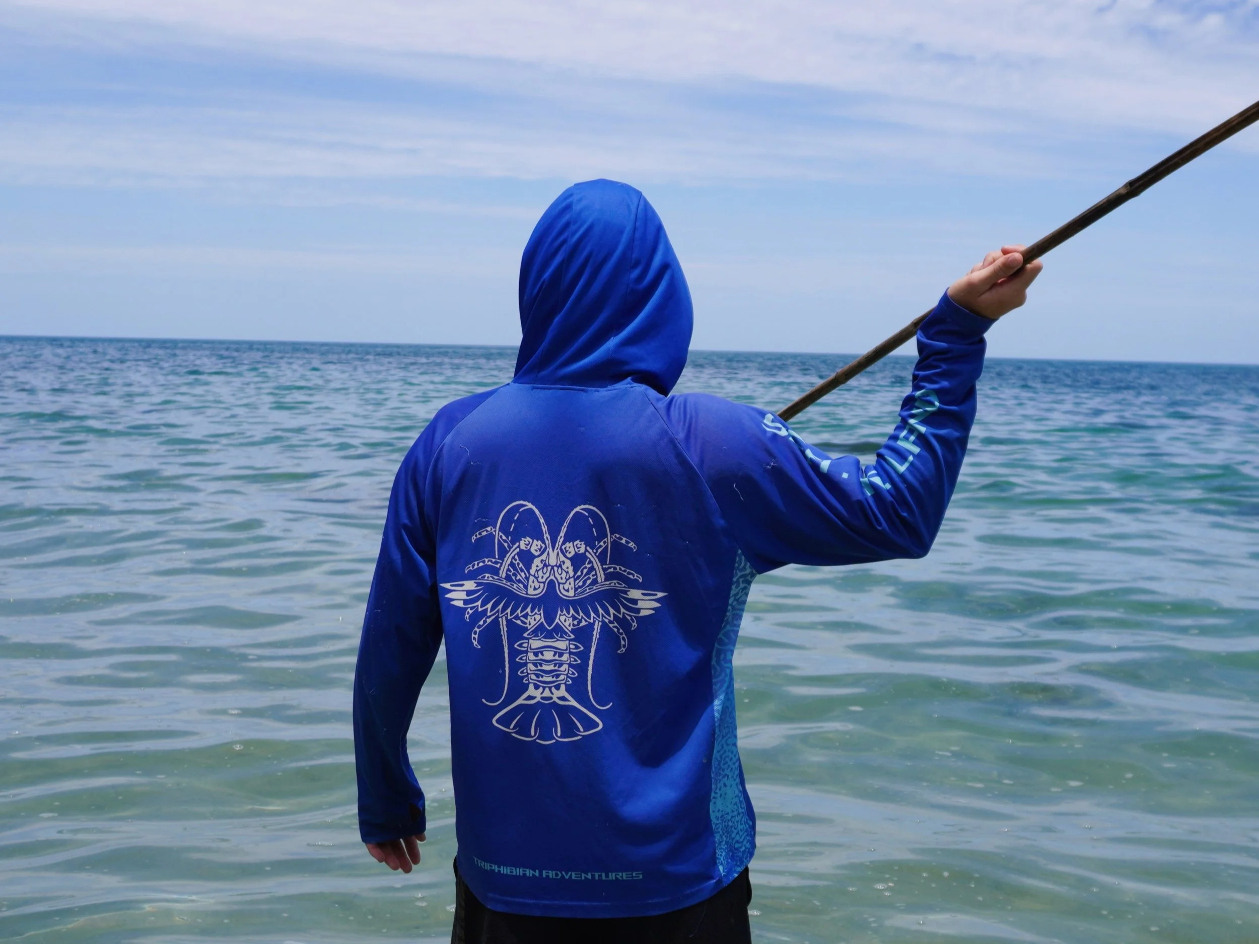 Man holding a hand spear while wearing a crayfish fishing shirt with a hood