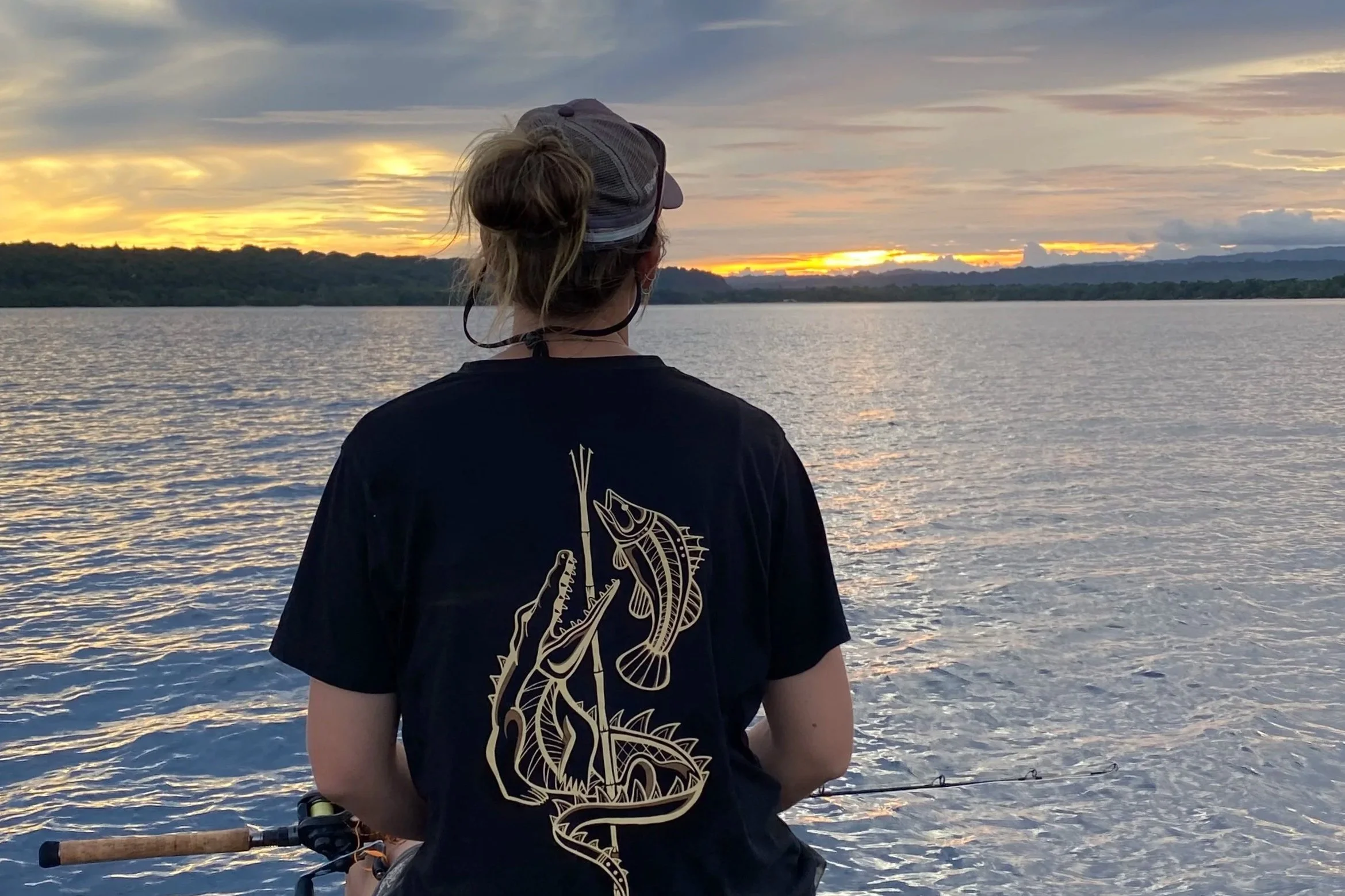 lady wearing a black shirt with a crocodile and barramundi image on the back. Also has an image of a hand spear on the design