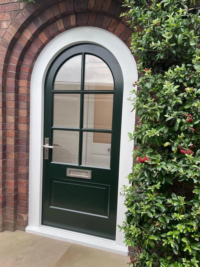 Arched green door with glass panels, set in a brick wall and surrounded by greenery.