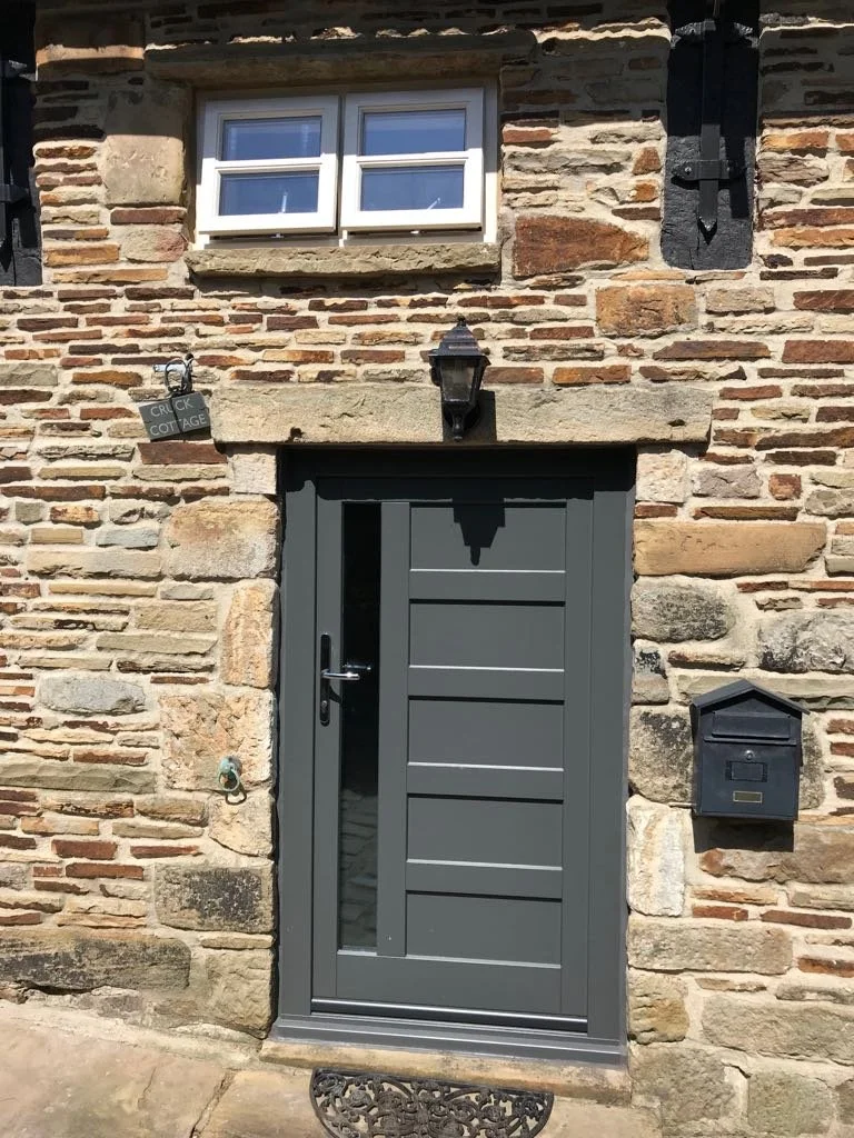 Stone cottage entrance with green door, mailbox, and lantern.
