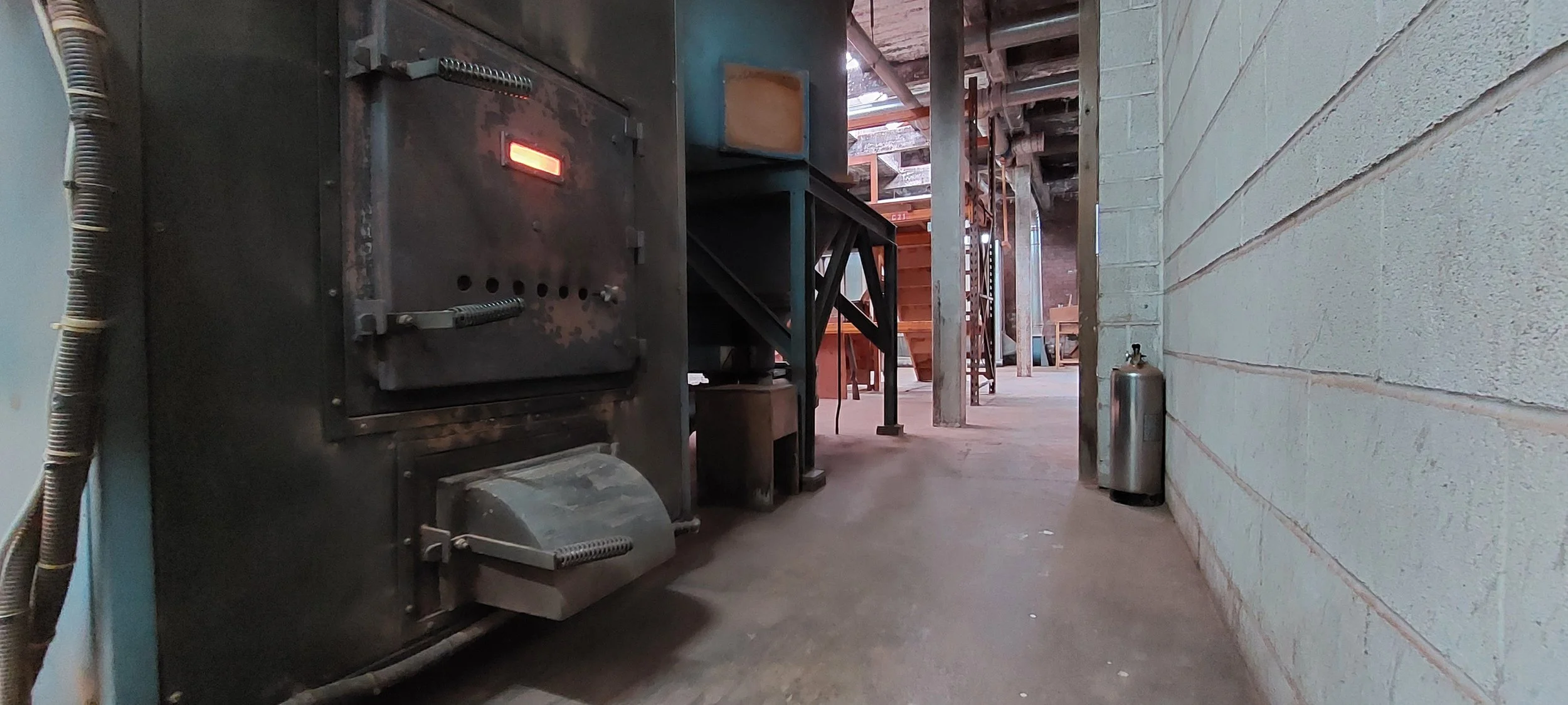 Industrial boiler room with metal furnace, pipes, and machinery in a warehouse setting.