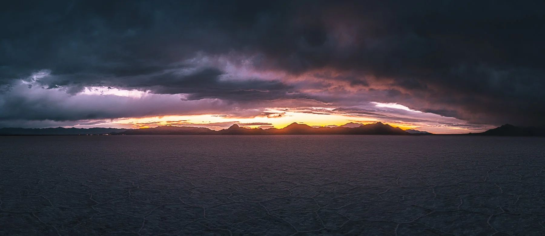 Panoramic image of the Bonneville Salt Flats in Utah during a storm with sunset in the distance behind the mountains.