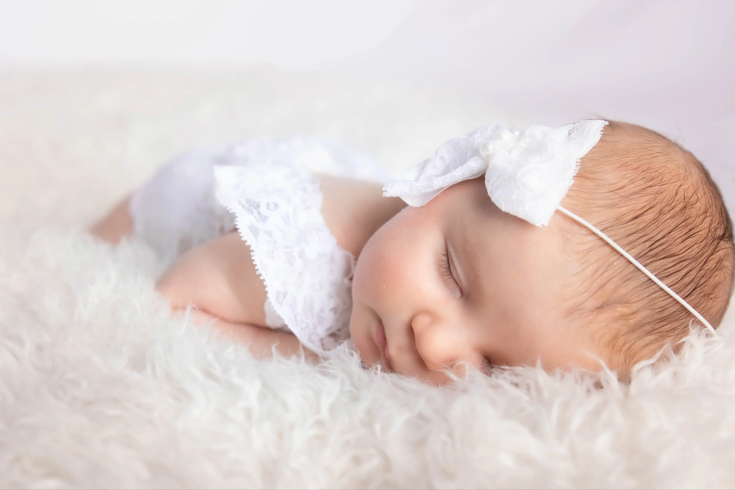 A close-up of a sleeping baby with a tissue on its head, lying on a fluffy white surface.