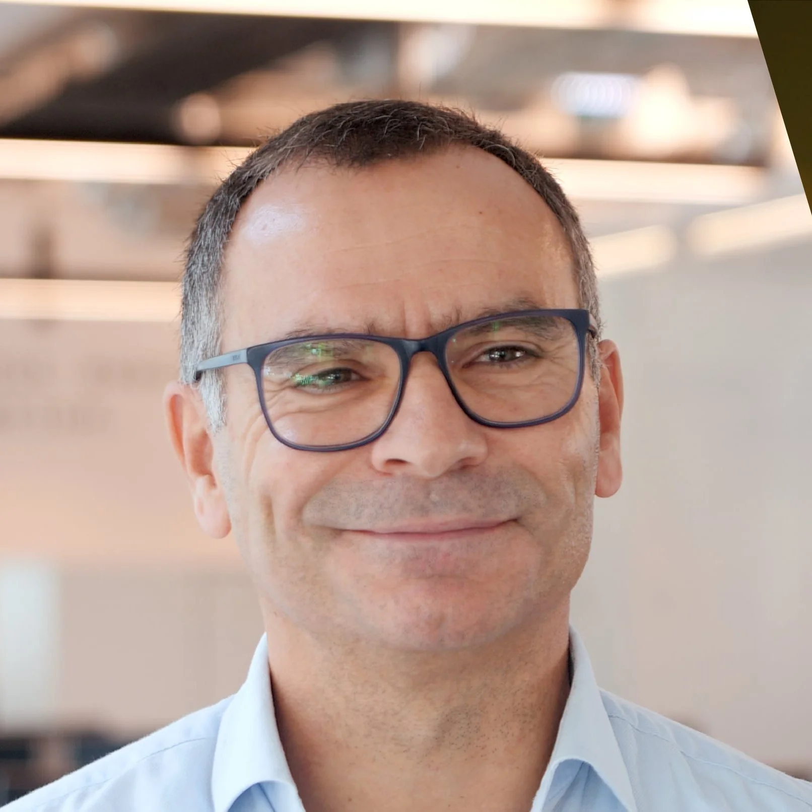 Homem de óculos sorrindo em ambiente de escritório.