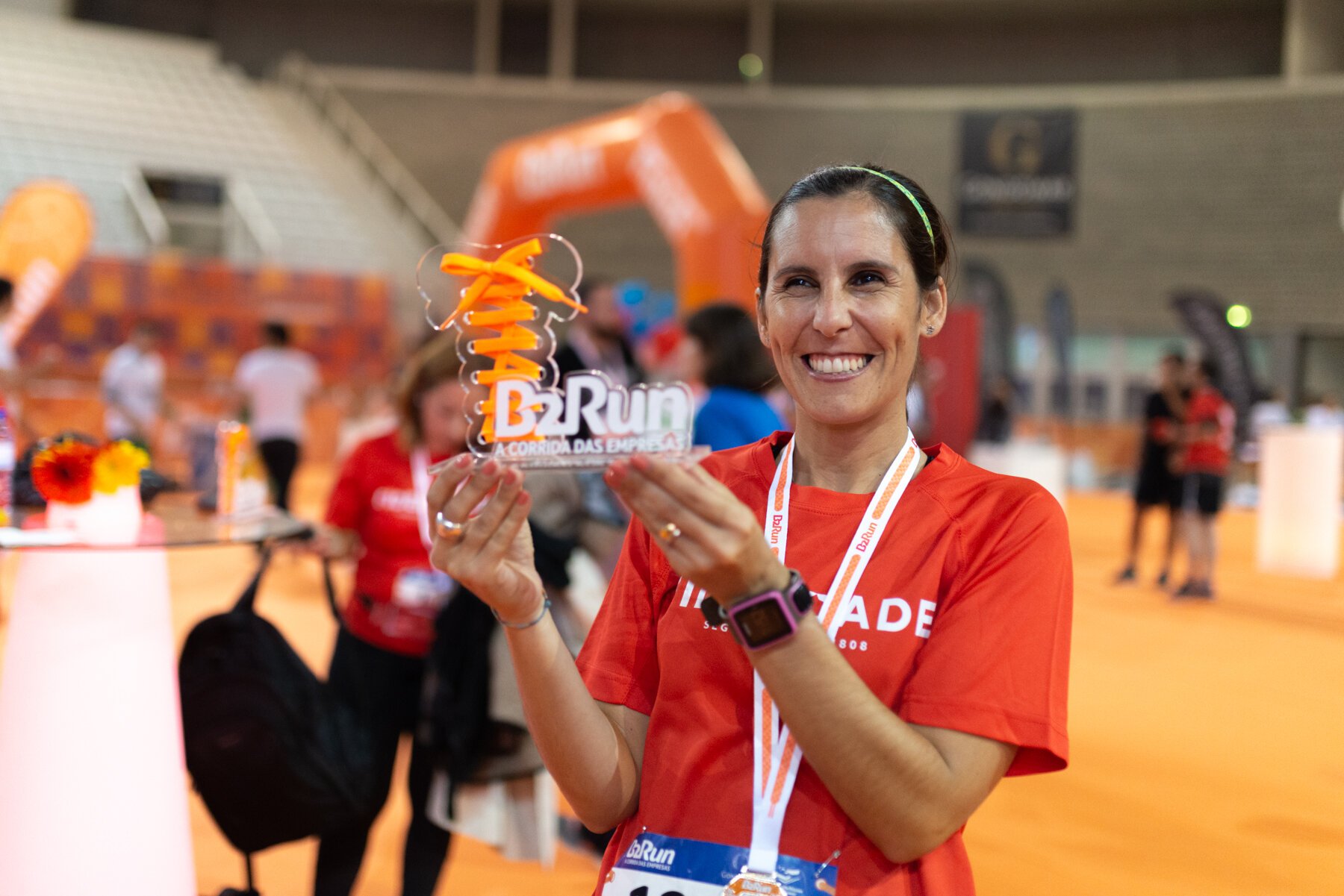 Mulher sorridente segurando troféu "B2Run a Corrida das Empresas" em evento esportivo.
