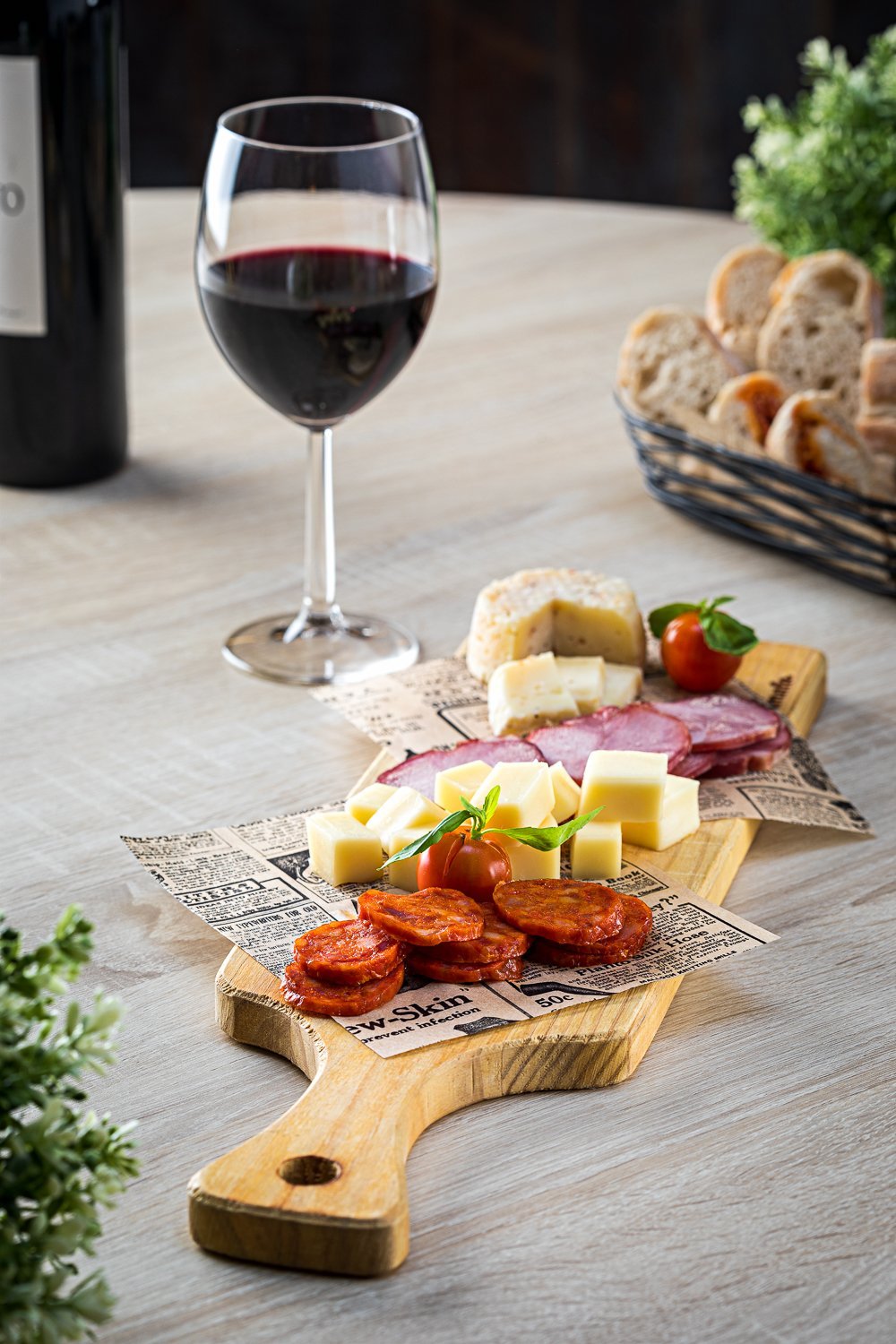 Tábua de frios com queijo, salame, chouriço, pão e tomate cereja, acompanhada de uma taça de vinho tinto.