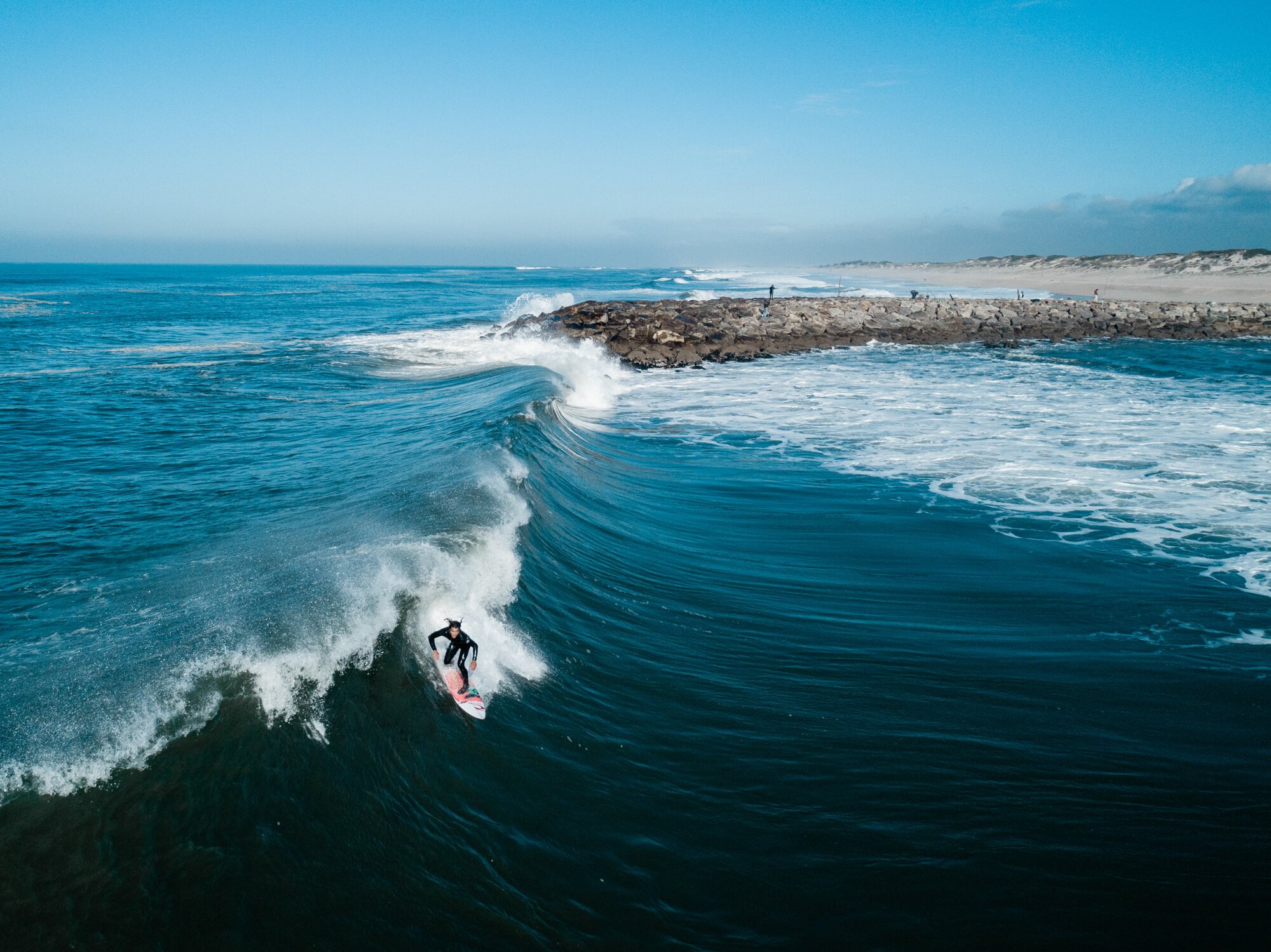 Surfista em onda grande no mar com costa arenosa ao fundo.