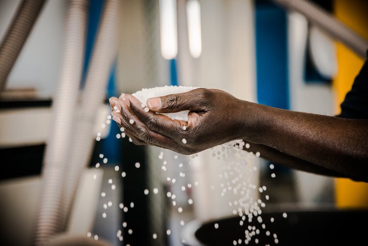 Mão segurando grãos brancos em ambiente industrial.