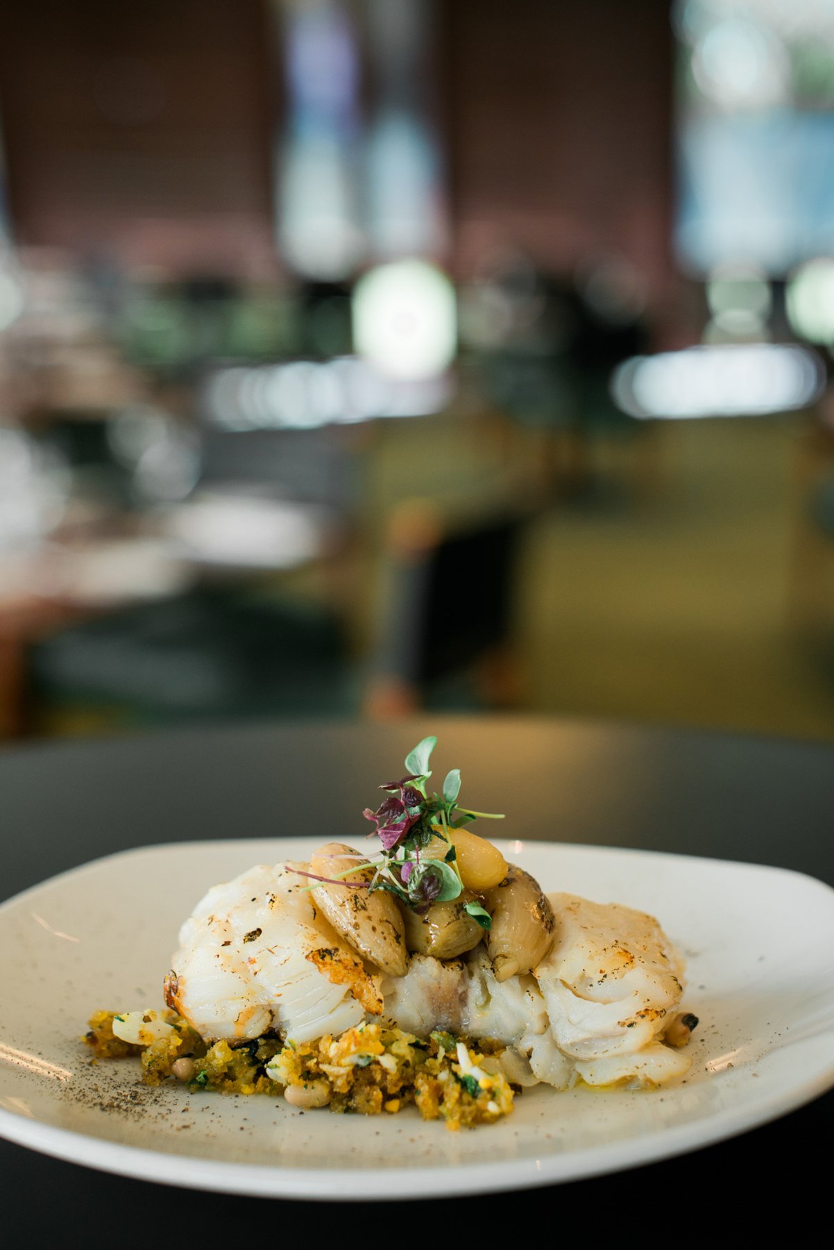 Prato de bacalhau assado com batatas e ervas, servido sobre migas, em um restaurante elegante.