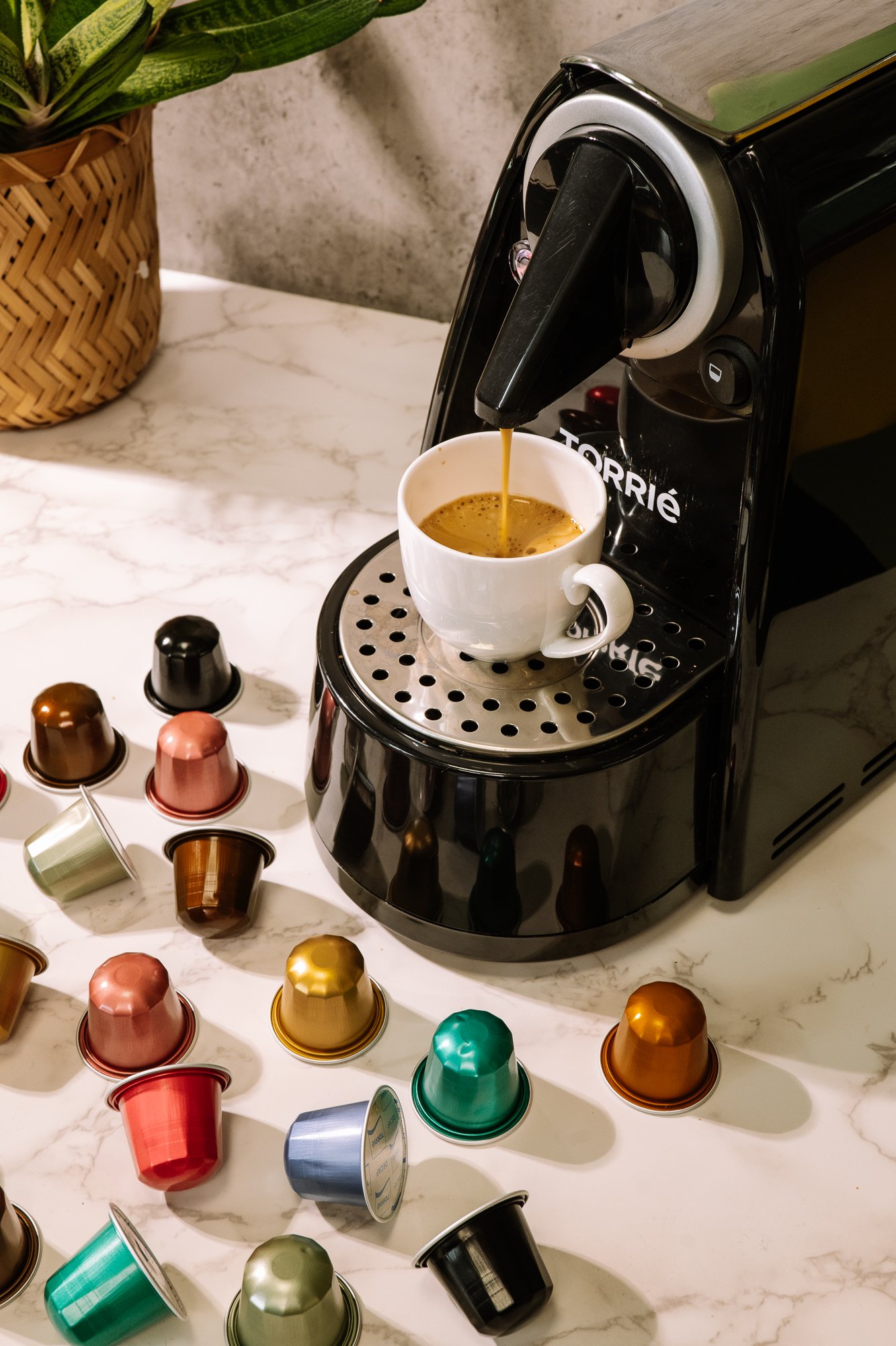 Máquina de café expresso com várias cápsulas multicoloridas ao redor e uma xícara sendo preenchida.