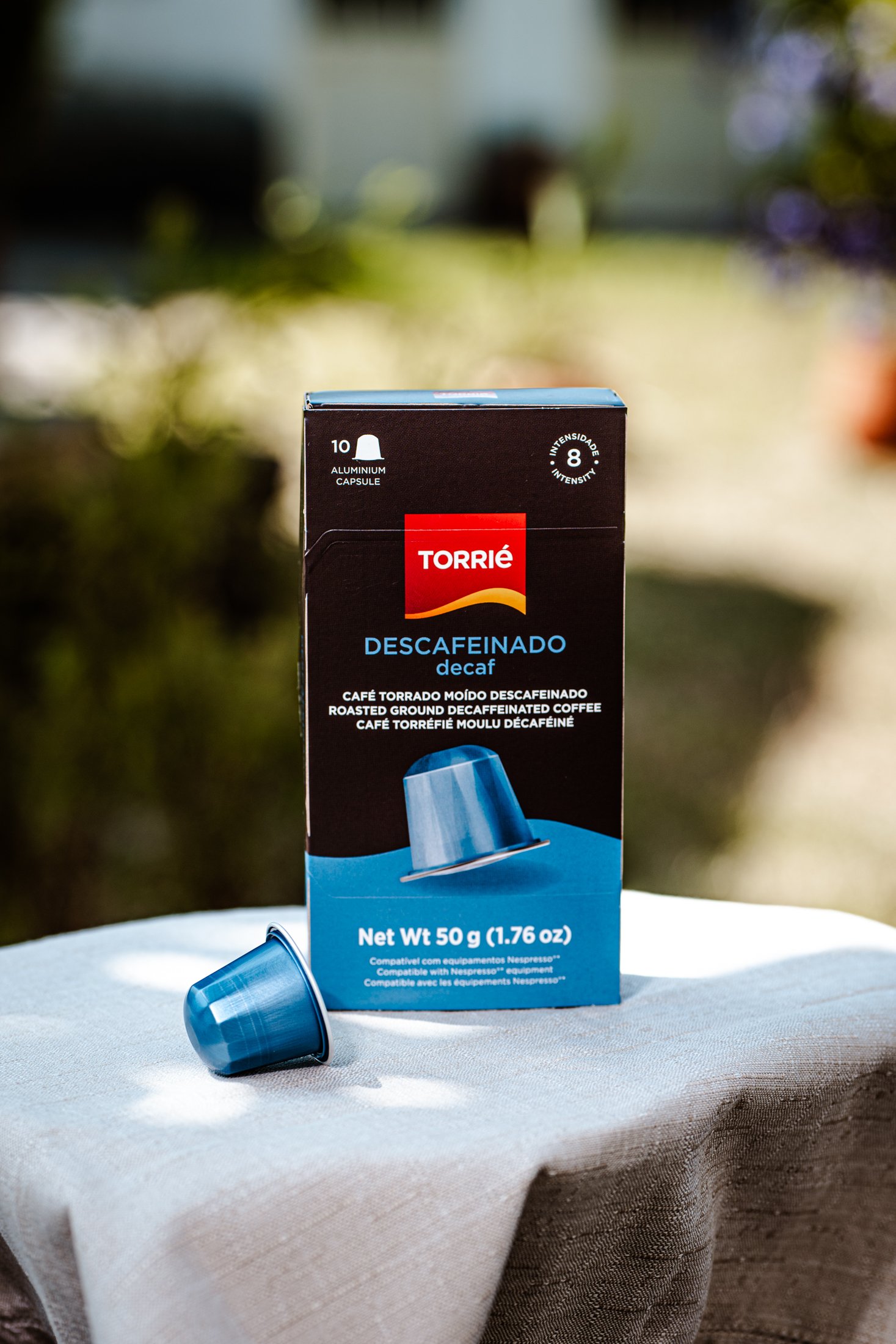 Caixa de cápsulas de café descafeinado Torrie em uma mesa, com uma cápsula azul na frente.