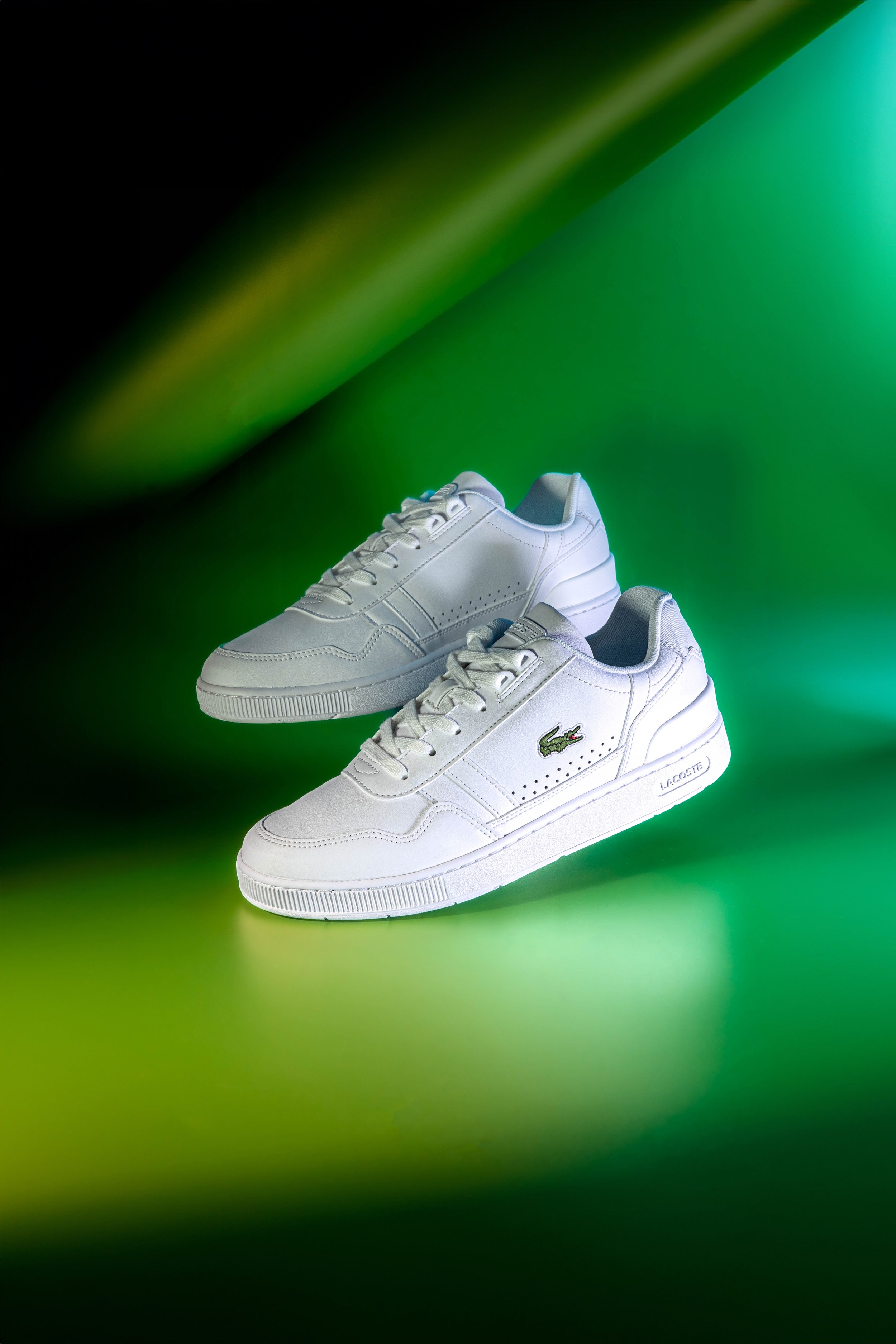 Tênis brancos da marca Lacoste em fundo verde iluminado.