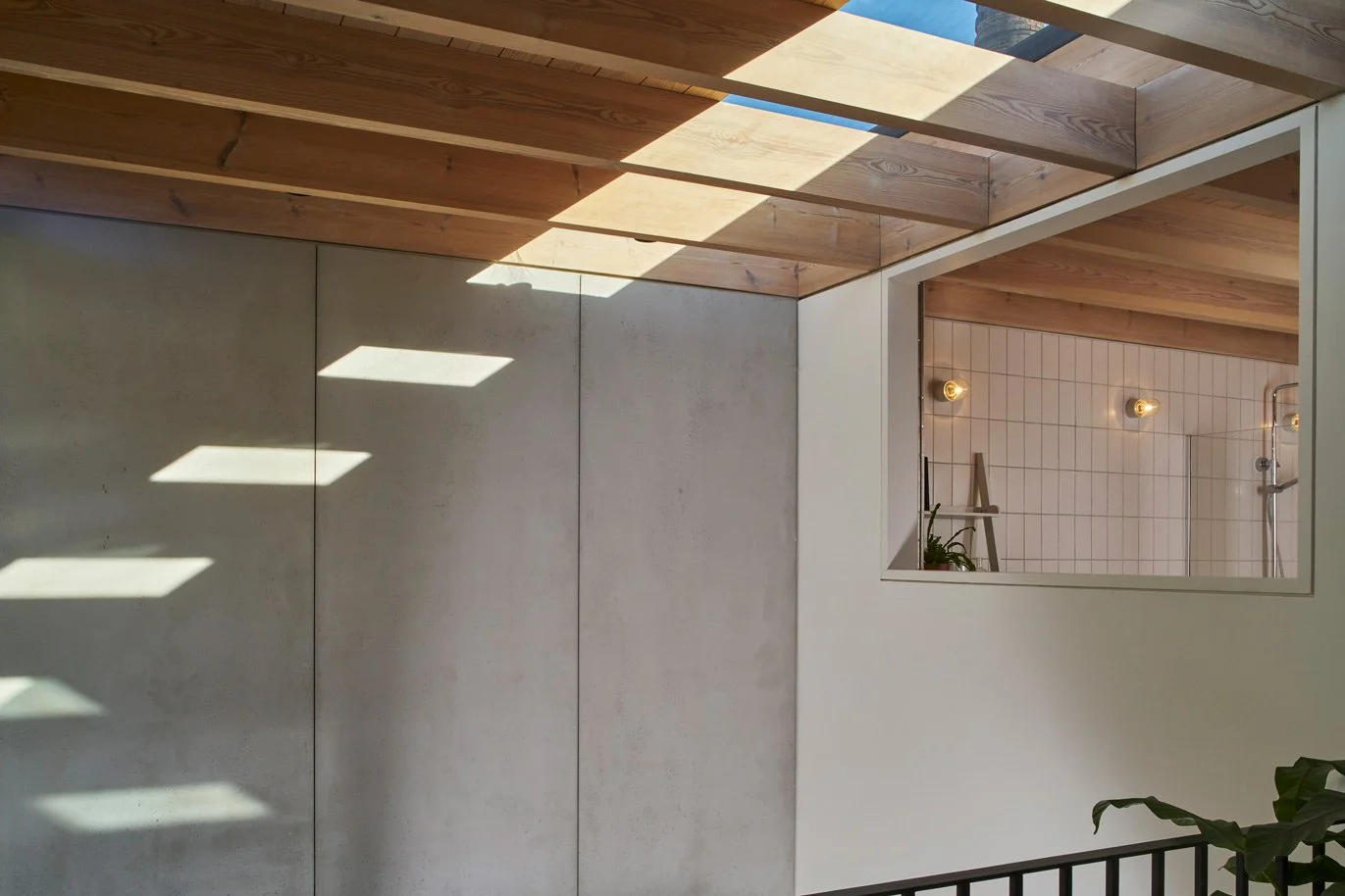 Light flooding into contemporary Gin Distillery converted interior in East London through exposed timber joists onto precast concrete walls with an internal window onto the black steel staircase