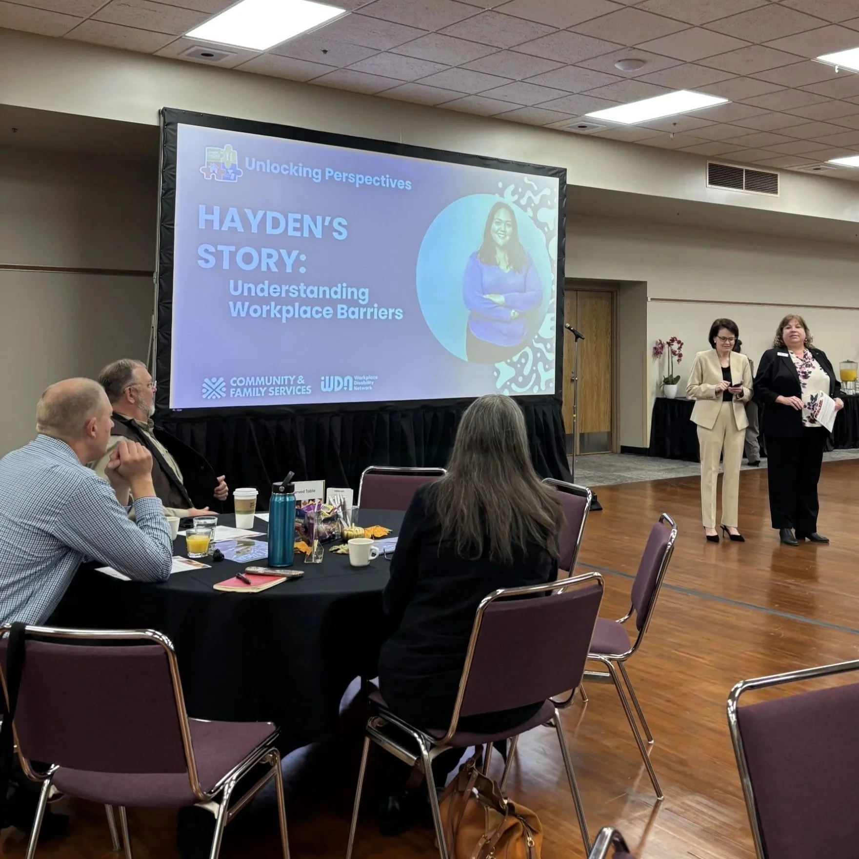 Attendees seated at tables during WDNBH’s Hayden’s Story NDEAM training, with presenters standing beside a projected slide reading “Hayden’s Story: Understanding Workplace Barriers.”
