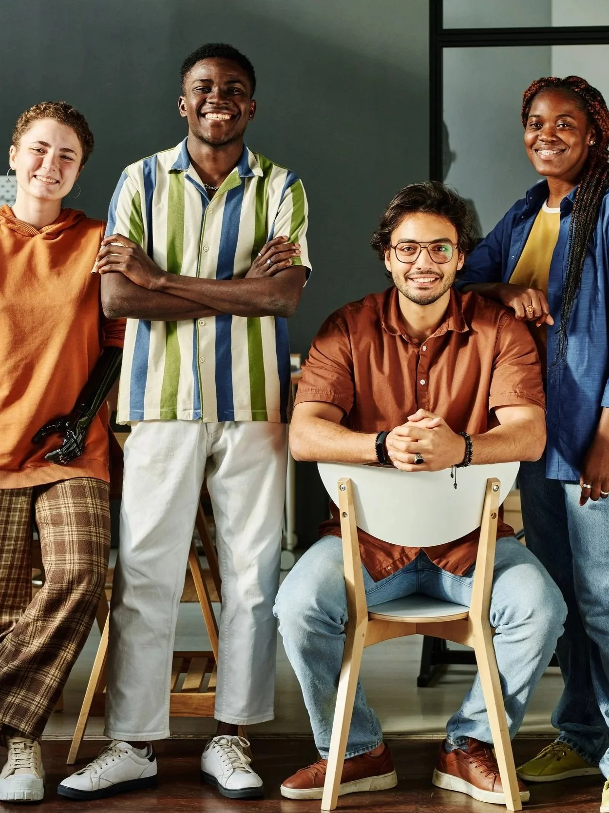 Group of four coworkers smiling and posing together in a modern office workspace.