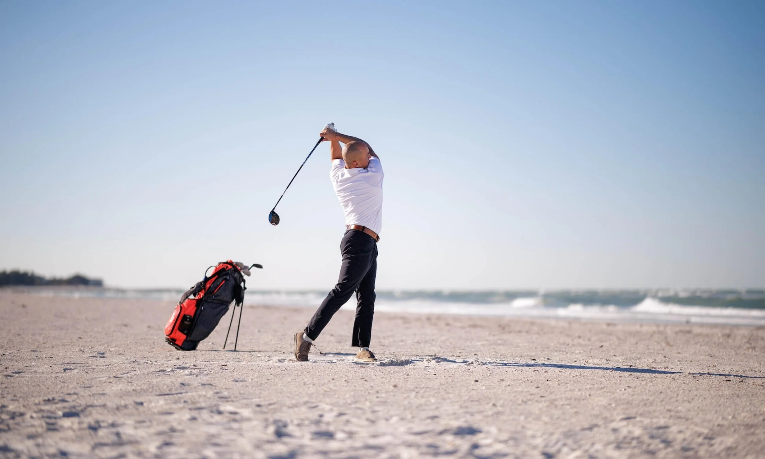 Golfer poses in follow-through on the beach