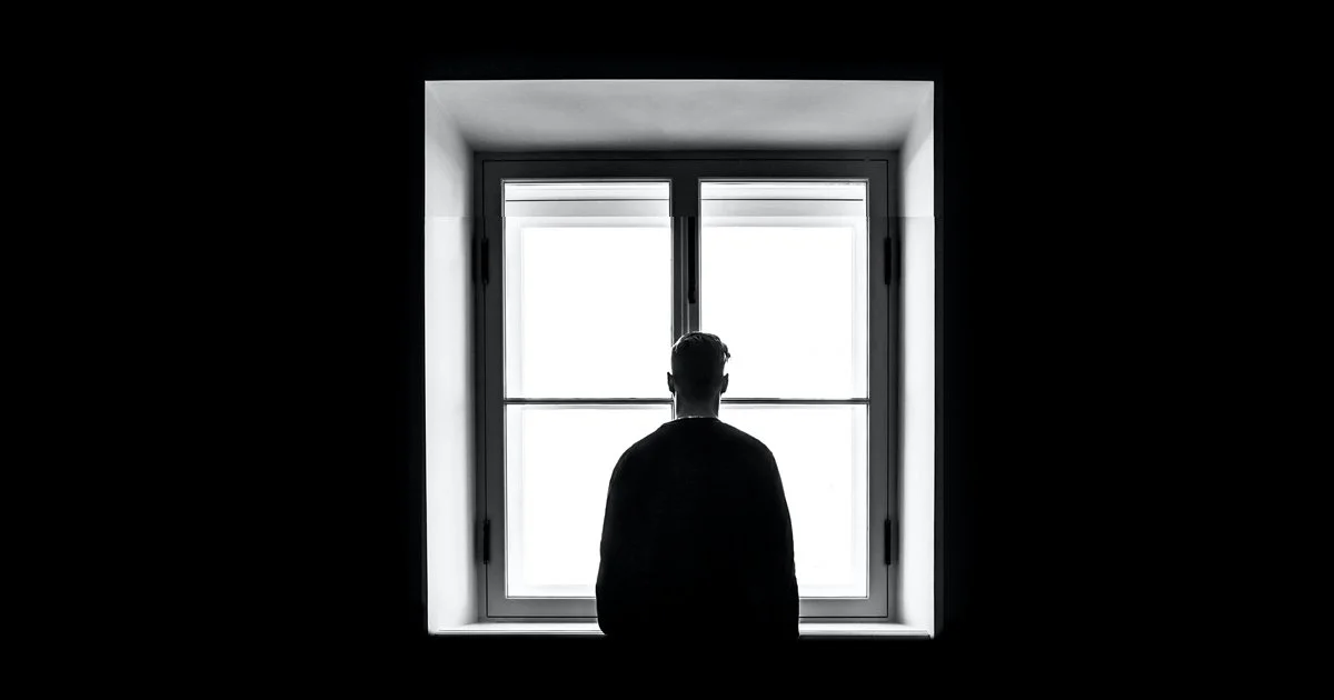 A man stands at a window thinking about public trust in charities.
